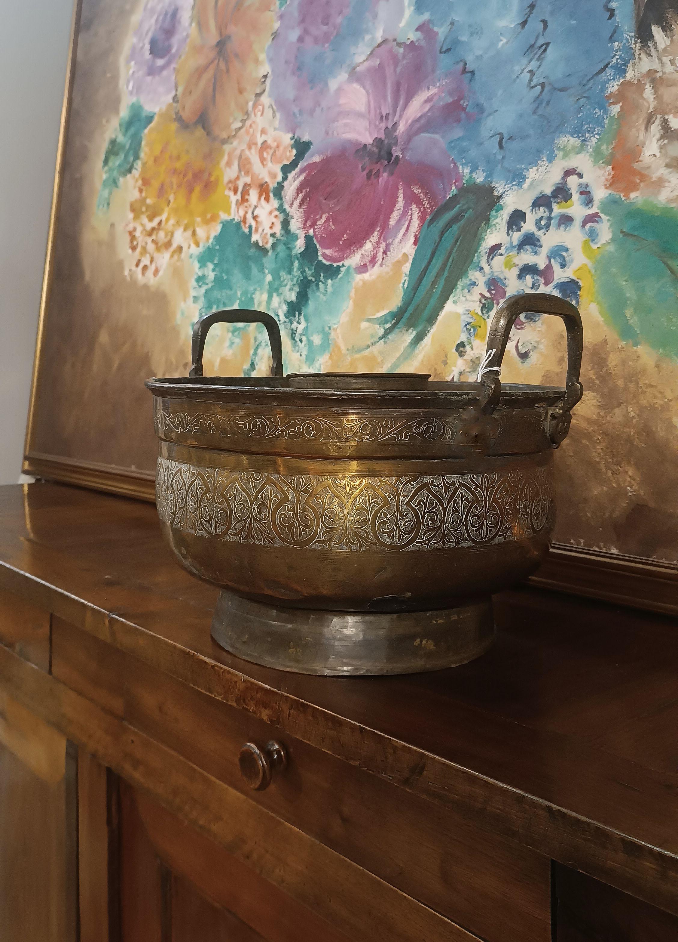 Ancient brass food warmer, worked and embossed by hand, characterized by an elegant and refined style. It has a round body supported by a ring foot, a lid with a handle and two handles to facilitate the grip. The decoration, made with the embossing