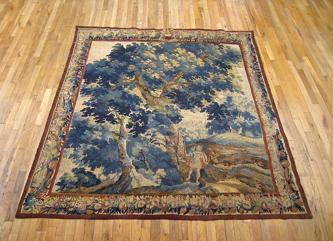 A Flemish Baroque landscape hunting tapestry from the late 17th or early 18th century, depicting a young Archer carrying a bow and arrow within a forest in a meadowland setting. Enclosed within a border of fruiting and flowering elements, with a