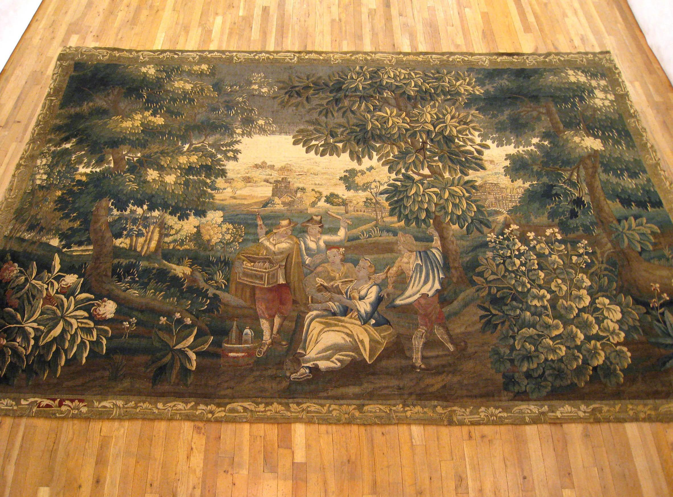 A Franco-Flemish rustic tapestry, possibly Lille or Aubusson, from the late 17th century, featuring a rustic scene with a group of people singing and playing music in a verdant setting. Large trees, plants, and flowers appear in the left and right