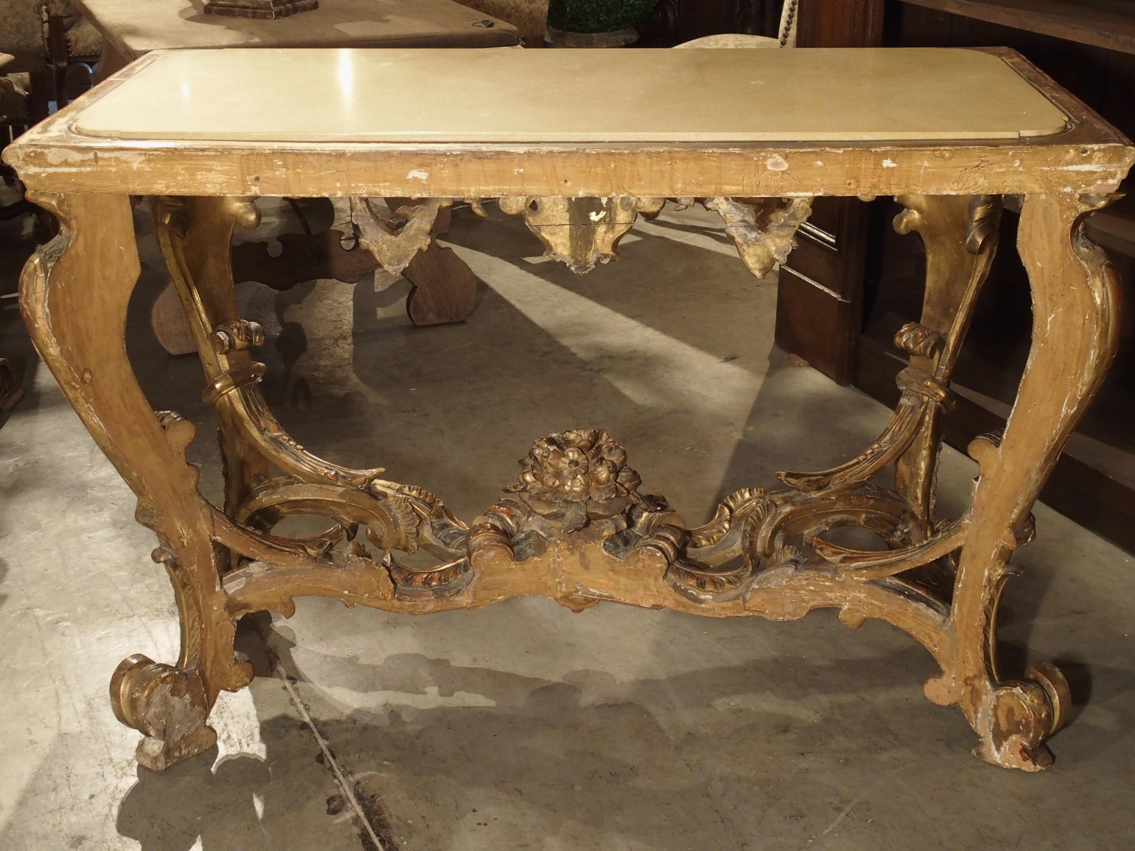 This Italian giltwood console is from the late 1600’s to the turn of the 18th century. It has a cream and beige colored inset marble top. This type of piece, with cabriole legs and shaped apron was directly inspired by French models, but the bolder