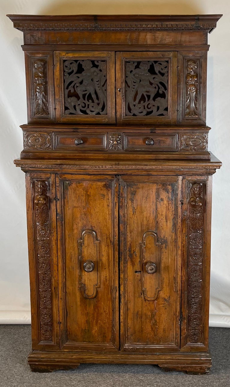 An elaborately carved Italian 17th C. (late Renaissance) two-part step-back cabinet; the upper portion having pierced metal cabinet doors in the form of frolicking cherubs above two drawers; the lower portion having two cabinet doors flanked by