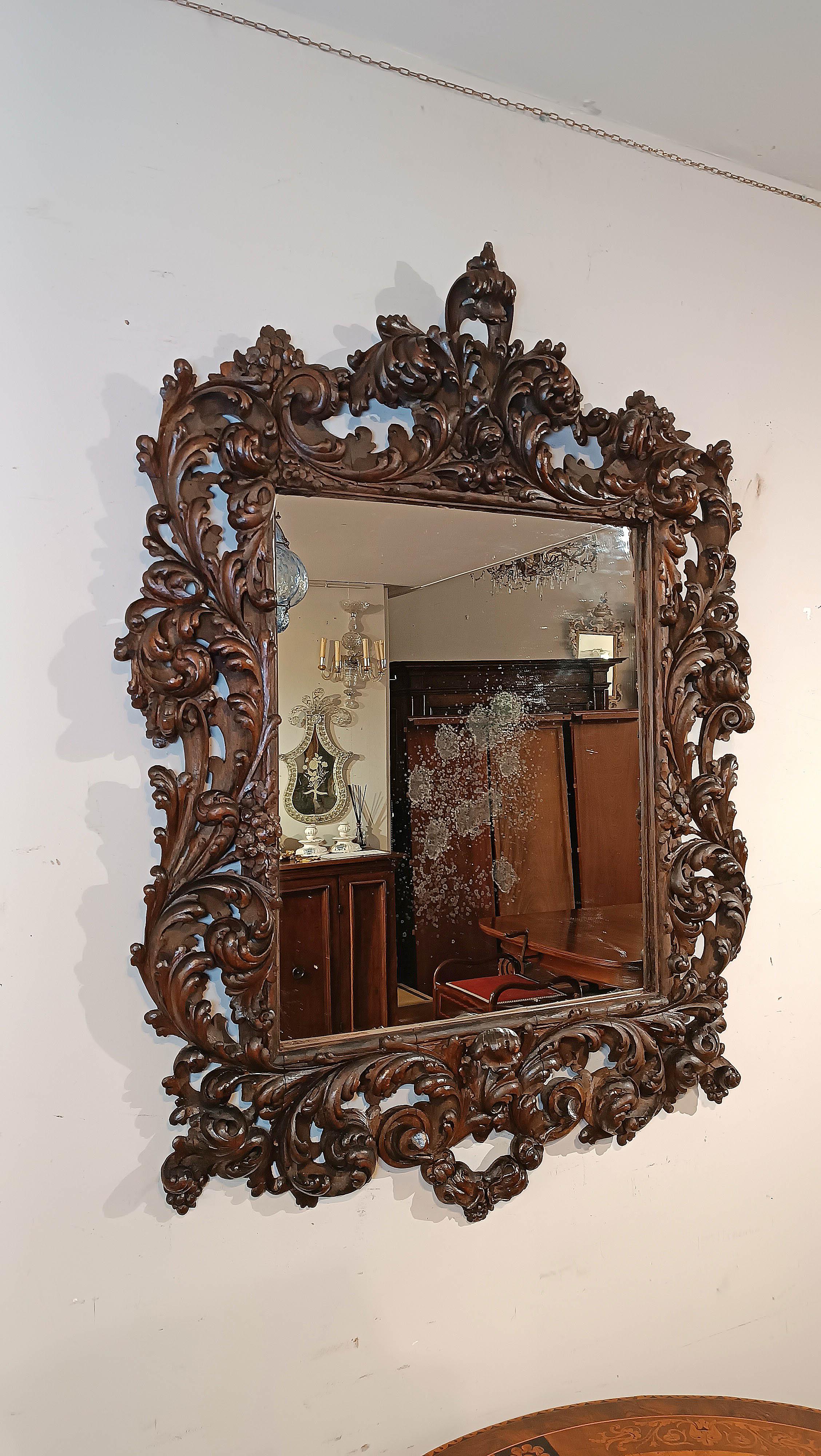 Refined mirror in solid walnut, hand-carved. The frame stands out for its elegance, embellished by the carving of plant motifs with spirals and small fruits that enhance its refinement. The cymatium also ends with a delicate curl. The mirror is in