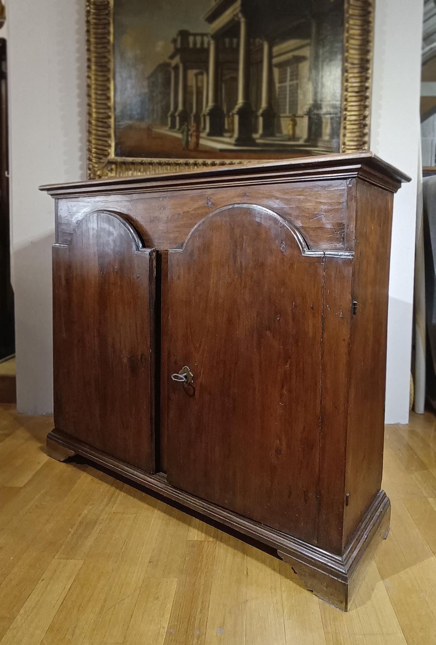 Splendid sideboard in solid walnut, finely hand-carved. It features bracketed feet and two double-lancet doors that lend harmony and elegance to the structure, opening onto three spacious internal shelves. The side hinges, expertly inserted into the