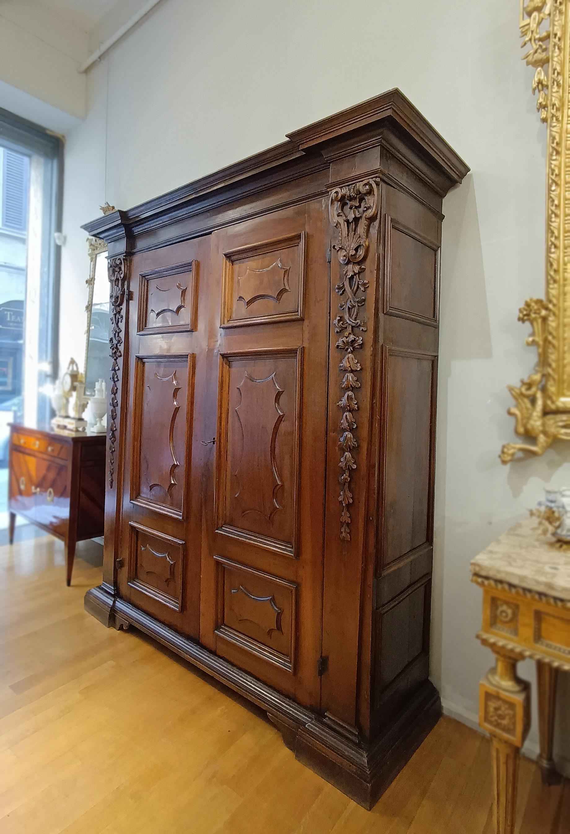 Elégante armoire en noyer massif, finement sculptée, qui représente une combinaison parfaite de fonctionnalité et d'esthétique. La structure est caractérisée par deux grandes portes d'entrée décorées de panneaux géométriques réalisés par des