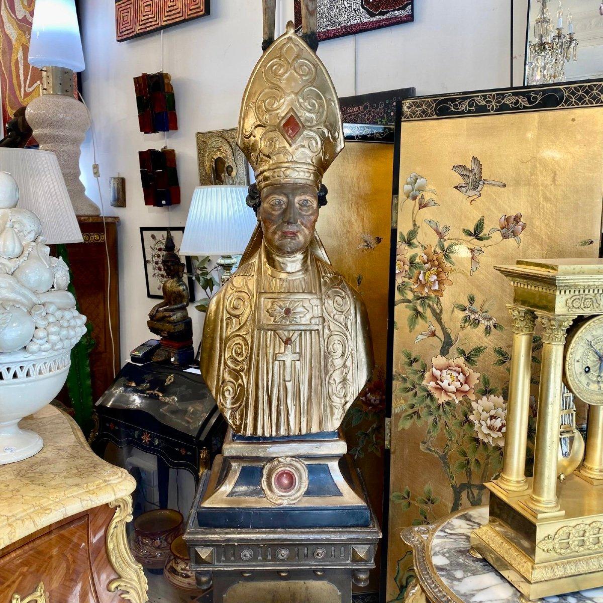 Diese außerordentlich majestätische und einzigartige, aus vergoldetem Holz geschnitzte Reliquienbüste stellt einen Bischof in einem goldenen Gewand dar. Der Torso ist in eine Toga gehüllt und gibt den Blick auf eine runde Vertiefung frei, in der