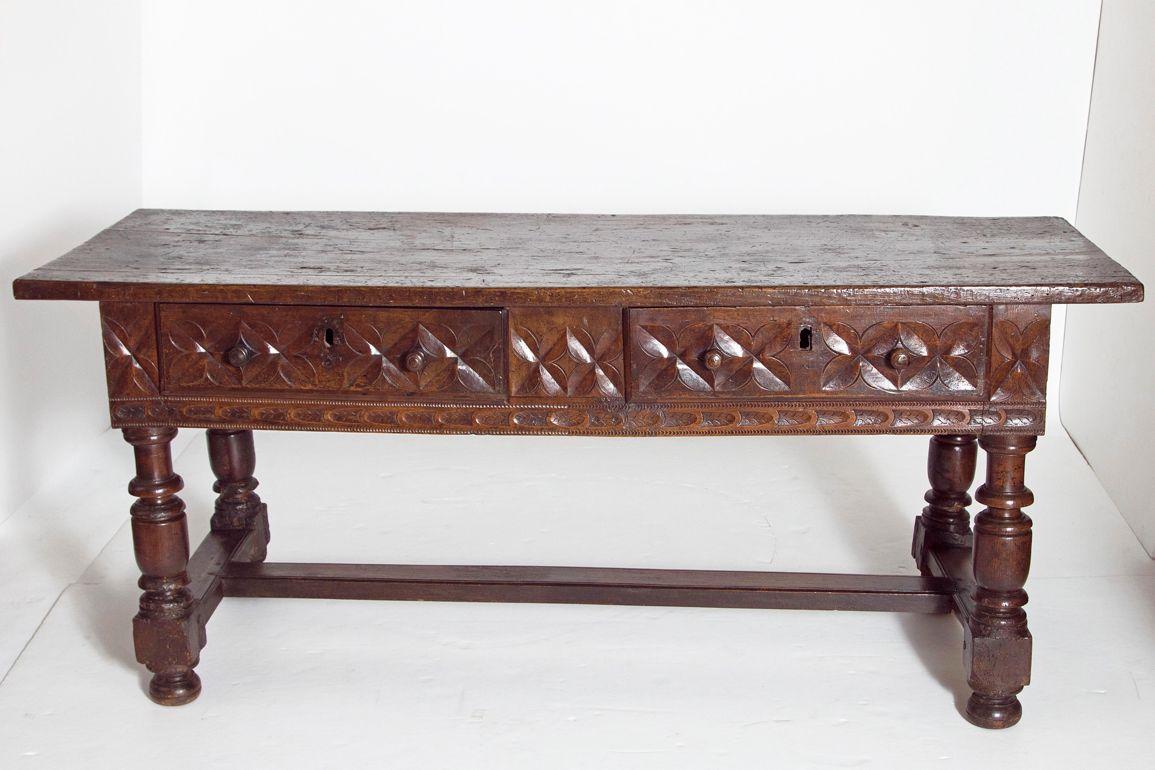 A large late 17th century Spanish hand carved walnut library or centre table with beautiful color and patina. The top is a single board above two drawers with wooden knobs and missing locks. The top shows an old patch repair, cracks and wear. The