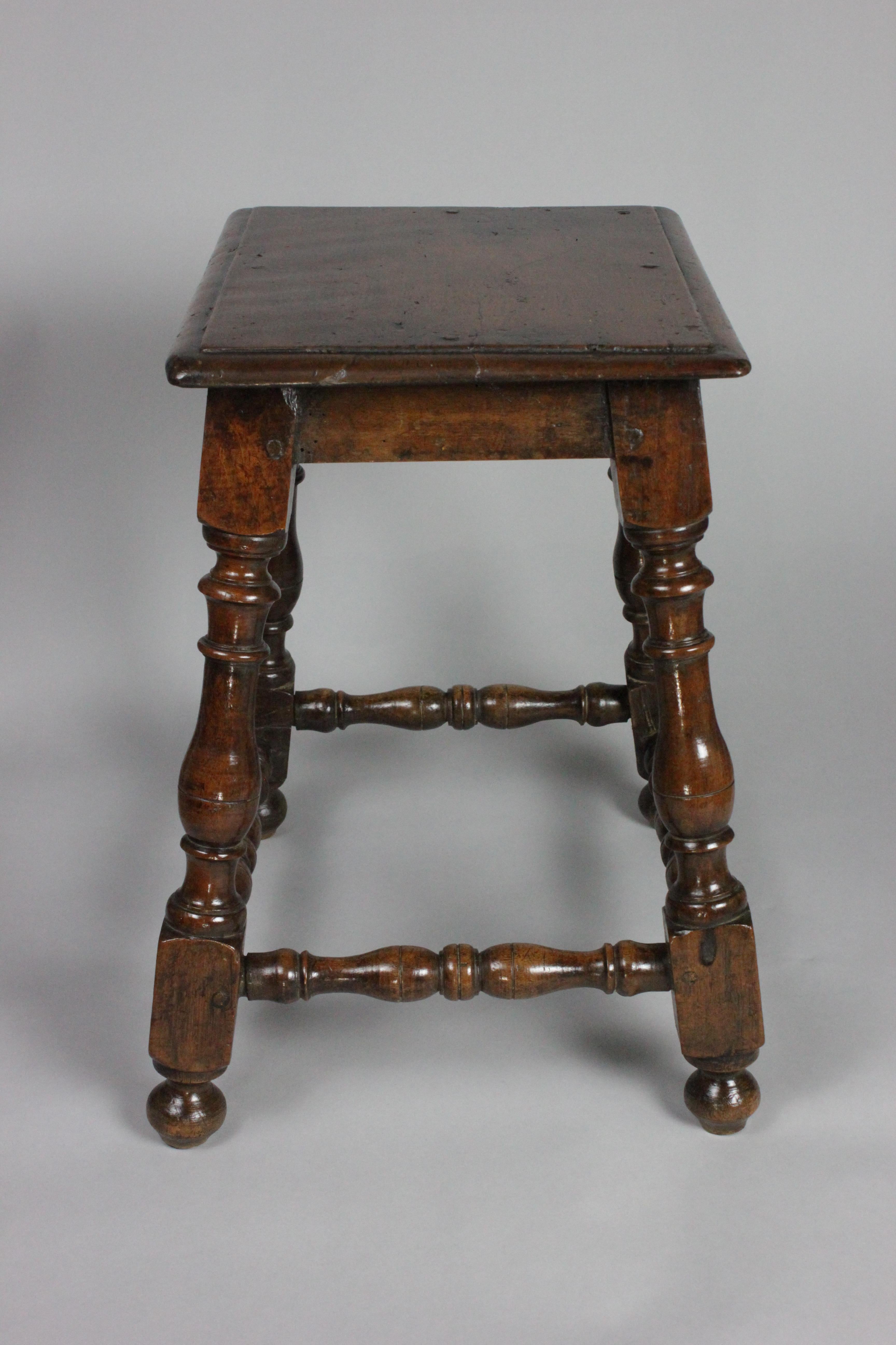 A decorative late 17th century Spanish walnut stool, circa 1680. Crafted with meticulous attention to detail, this stool showcases the rich beauty of walnut, gracefully shaped into an elegant design. The finely turned legs and sturdy stretchers add