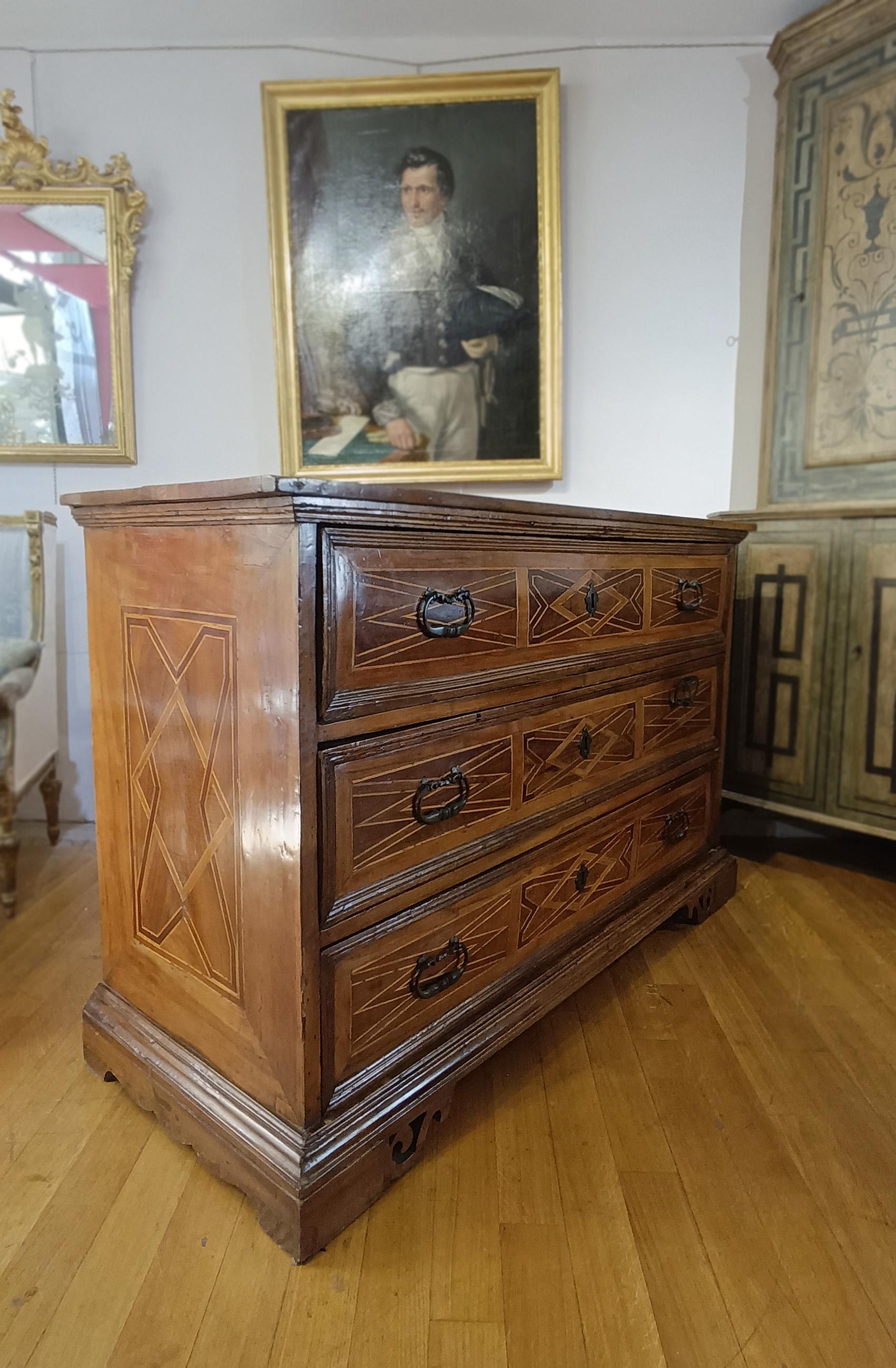 Elegant walnut chest of drawers, hand-carved and embellished with fruitwood inlays. The piece features three ergonomic drawers, ideal for storing objects, decorated on the front with refined geometric inlays that enhance its elegance; geometric