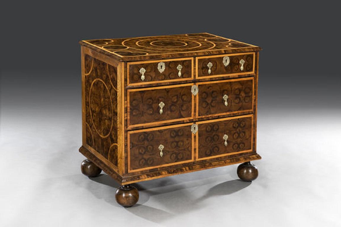 The rectangular top is laid with a central circular geometric pattern of cut oyster veneers bordered with inlaid Holly stringing with a heart shaped pattern to each corner and is cross-banded and has a shaped moulded edge. 

Each side of the chest