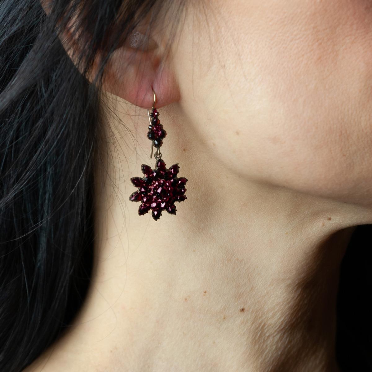 Late 1800s 9 kt yellow gold antique earrings with bright red faceted Bohemian garnets, characterized by an intense color. The earrings are composed by a small central round garnet and several garnets around  composing a flower shape.
An ancient