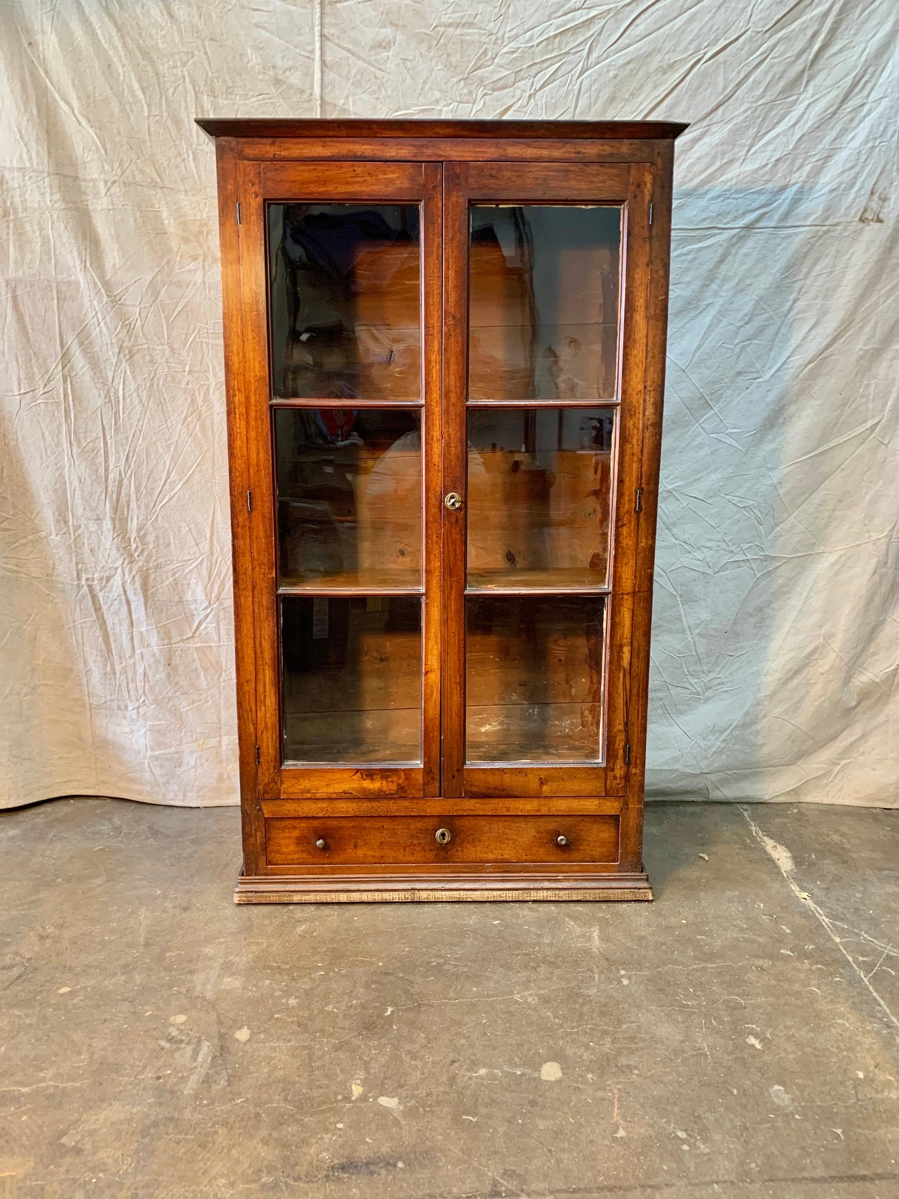 Found in the South of France, this handsome Walnut Glass Front Display Cabinet or Bookcase was crafted from old growth walnut by French artisans in the late 1800s. The piece features two glass paneled doors that open to reveal two adjustable shelves