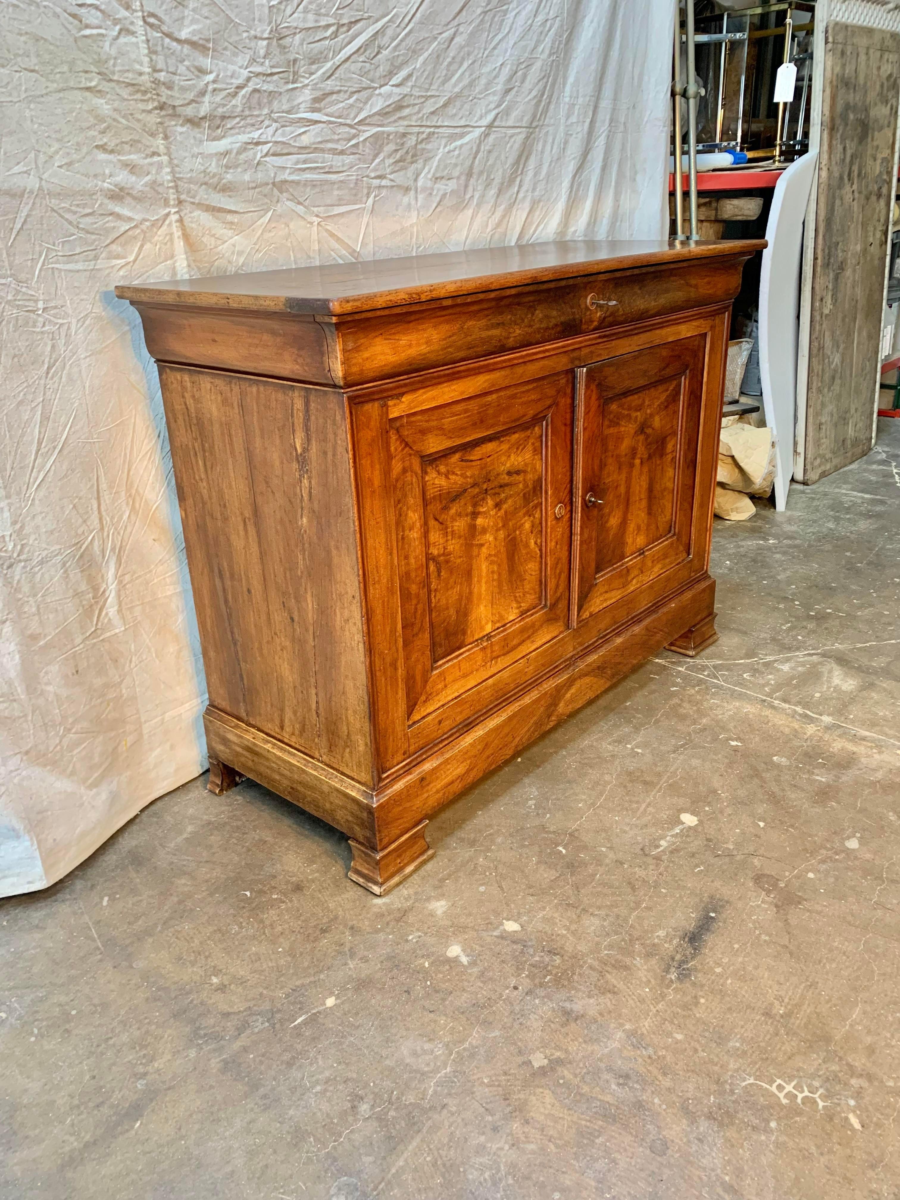 Found in the South of France, this Late 1800s French Walnut Louis Philippe Sideboard is constructed from old growth walnut. The piece features a banded top resting over a front single drawer. The two book matched doors open to reveal shelving and