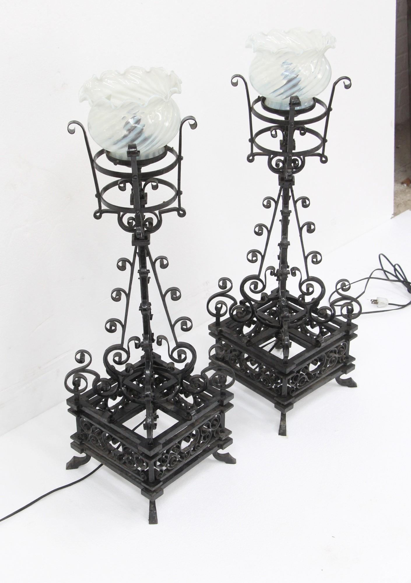 Late 1800s tall table lamps made from hand forged black wrought iron. Featuring fine intricate details on the wrought iron. The included hand blown shades were added later. Originally gas lights but now electrified. Cleaned and rewired. Priced as a