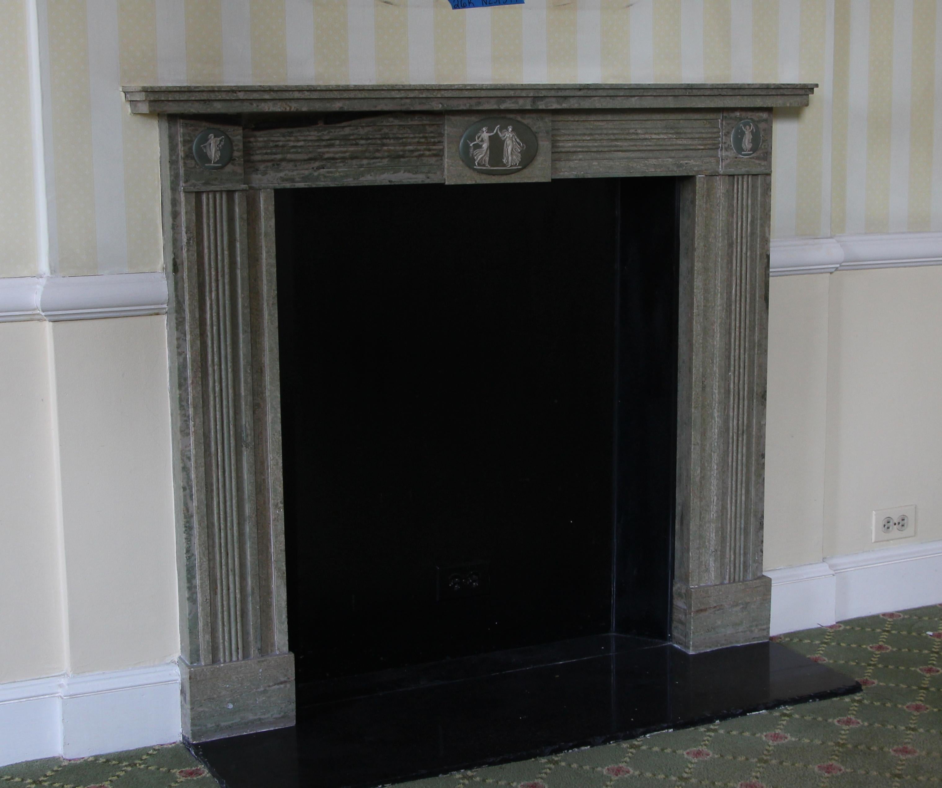 Hearth not included. 19th century petite English Regency style gray marble mantel with carved figural motifs on the two top plinths and the middle of the header and gray veining. Fluted carving on breast plate and pilasters on sides. This mantel was
