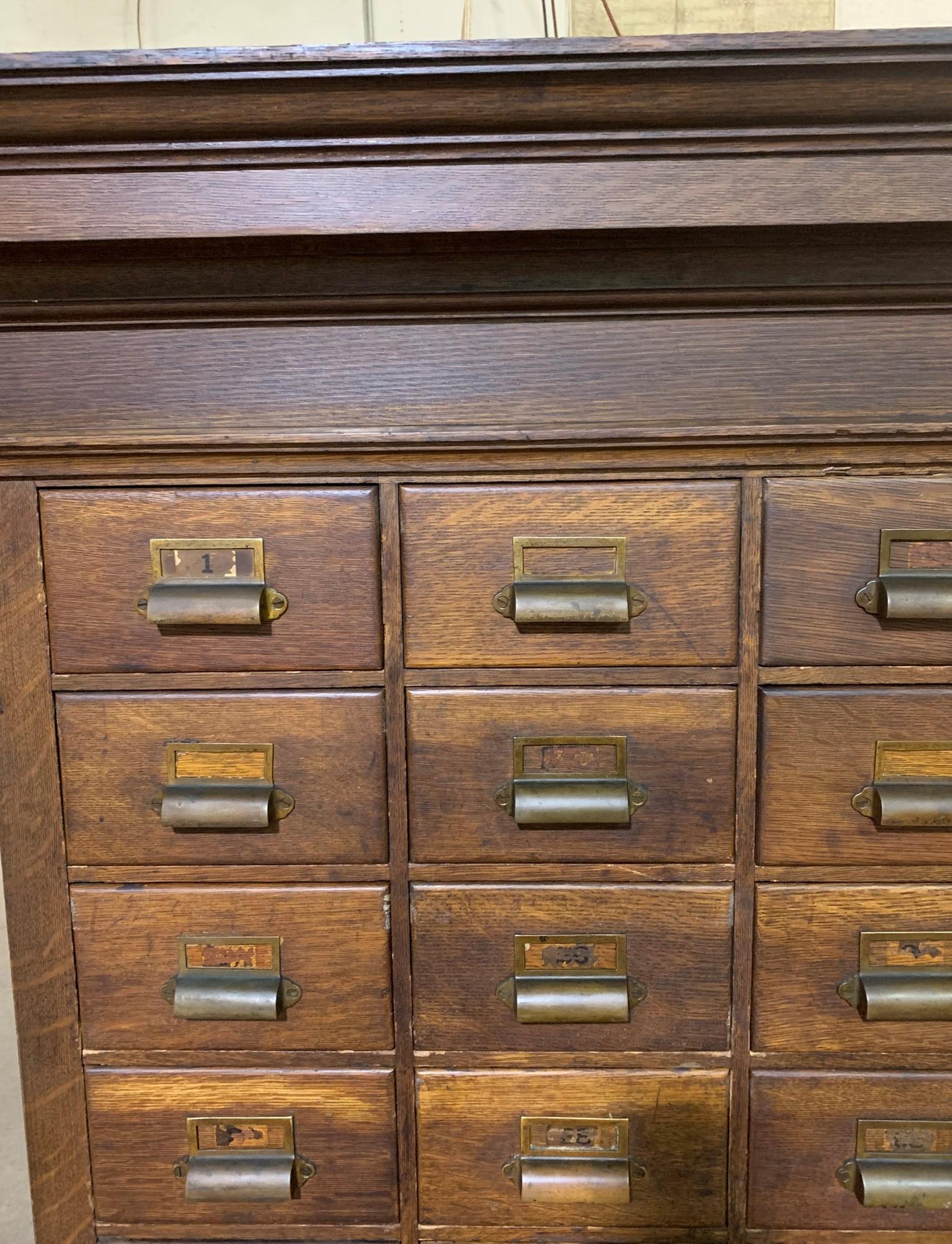 Massachusetts Industrial oakwood apothecary cabinet from the late 1800s. This comes in an upper and lower section. There are 108 catalog drawers in the upper part and three bottom sections in the lower part. This piece has been recently restored.