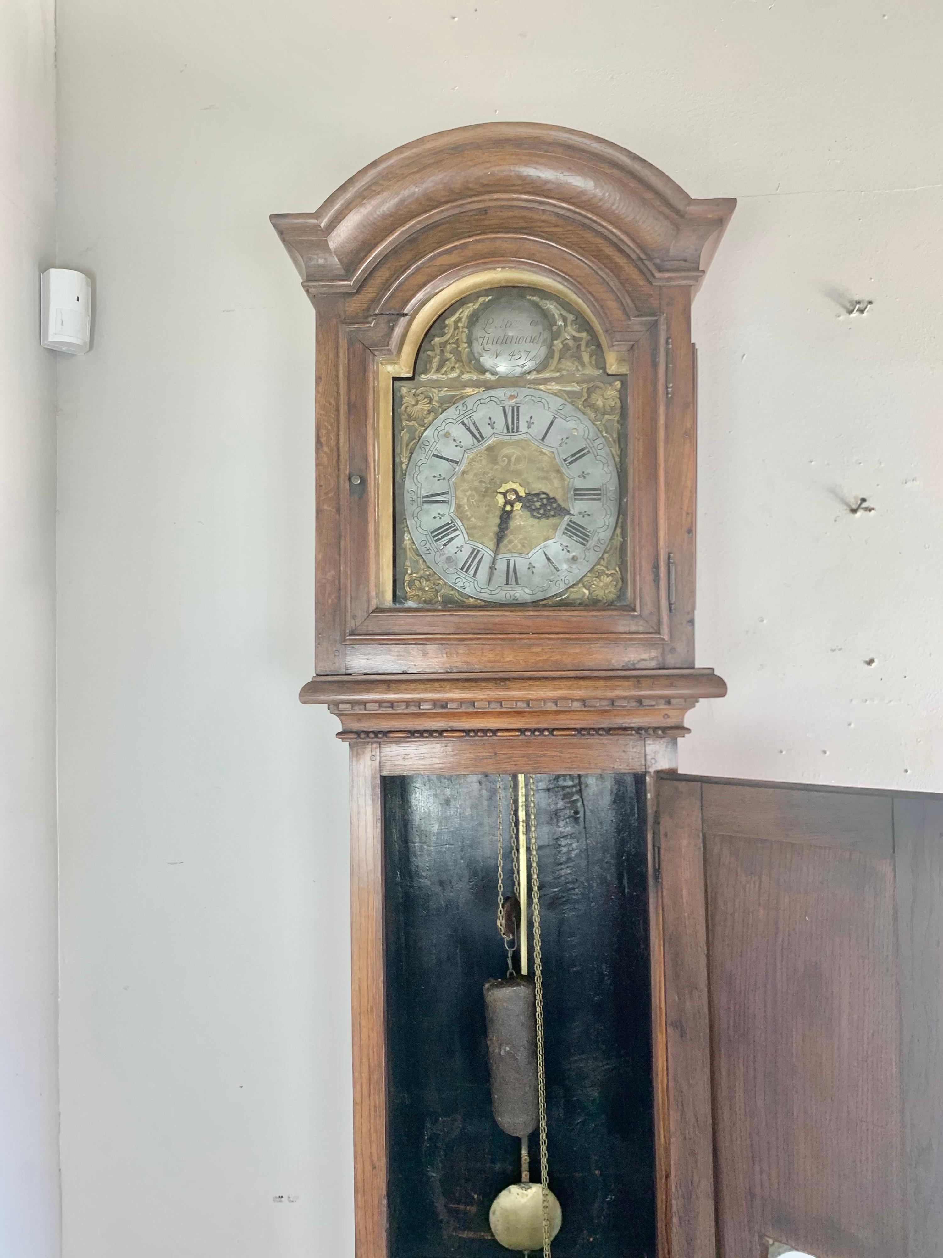 Late 18th century Belgium provincial long case clock with inlaid star motif at the bottom.  The clock retains al of it's original hardware.  The door with pendulum window opens to reveal a single weighted pendulum.  The top has an arched and carved