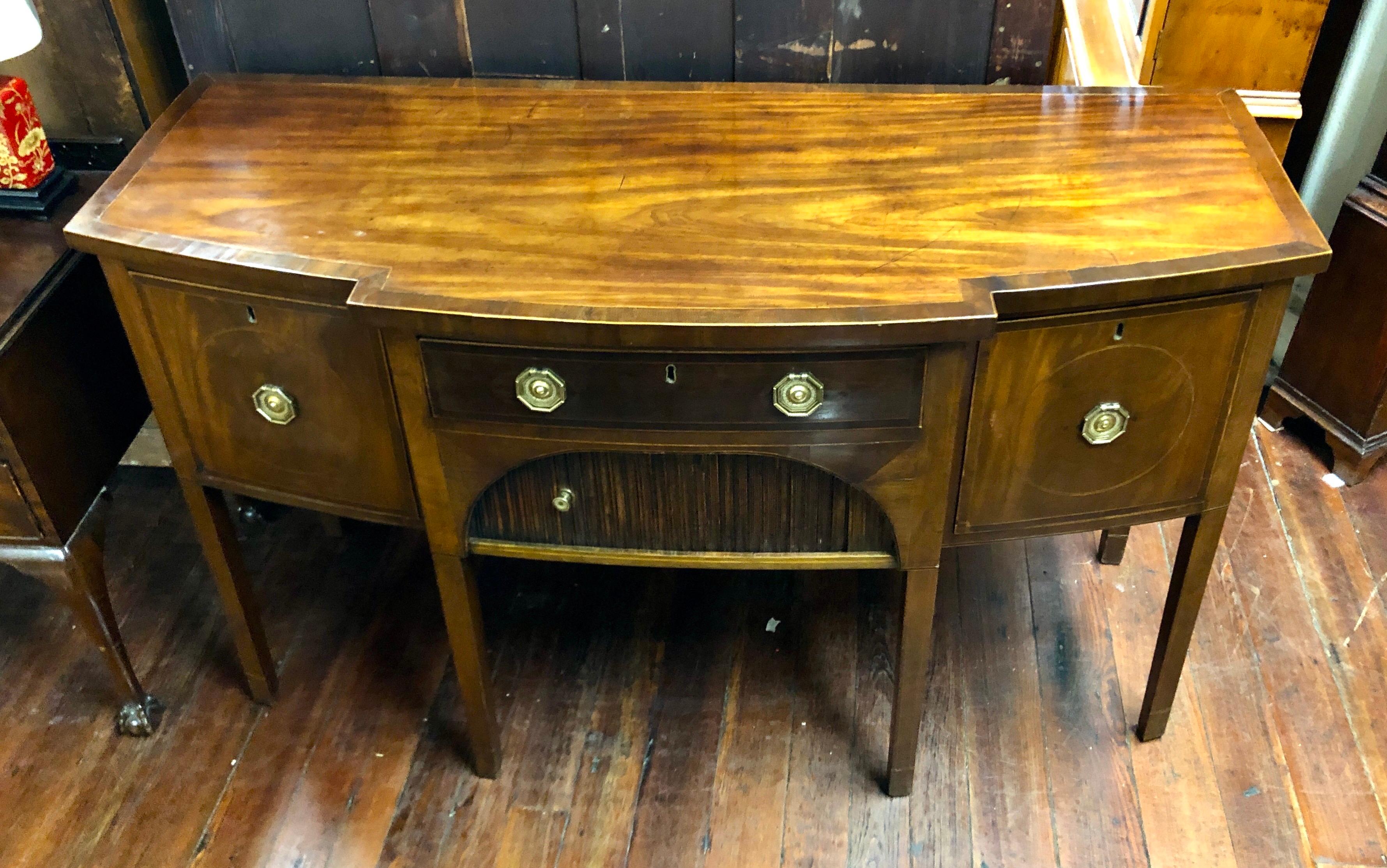 A wonderful, rare period Geo. III late 18th/early 19th century inlaid mahogany sideboard with its original tambour ribbed, sliding cupboard. It has a central drawer flanked by two deep, cellarette drawers. The brasses are antique and quite fine, but