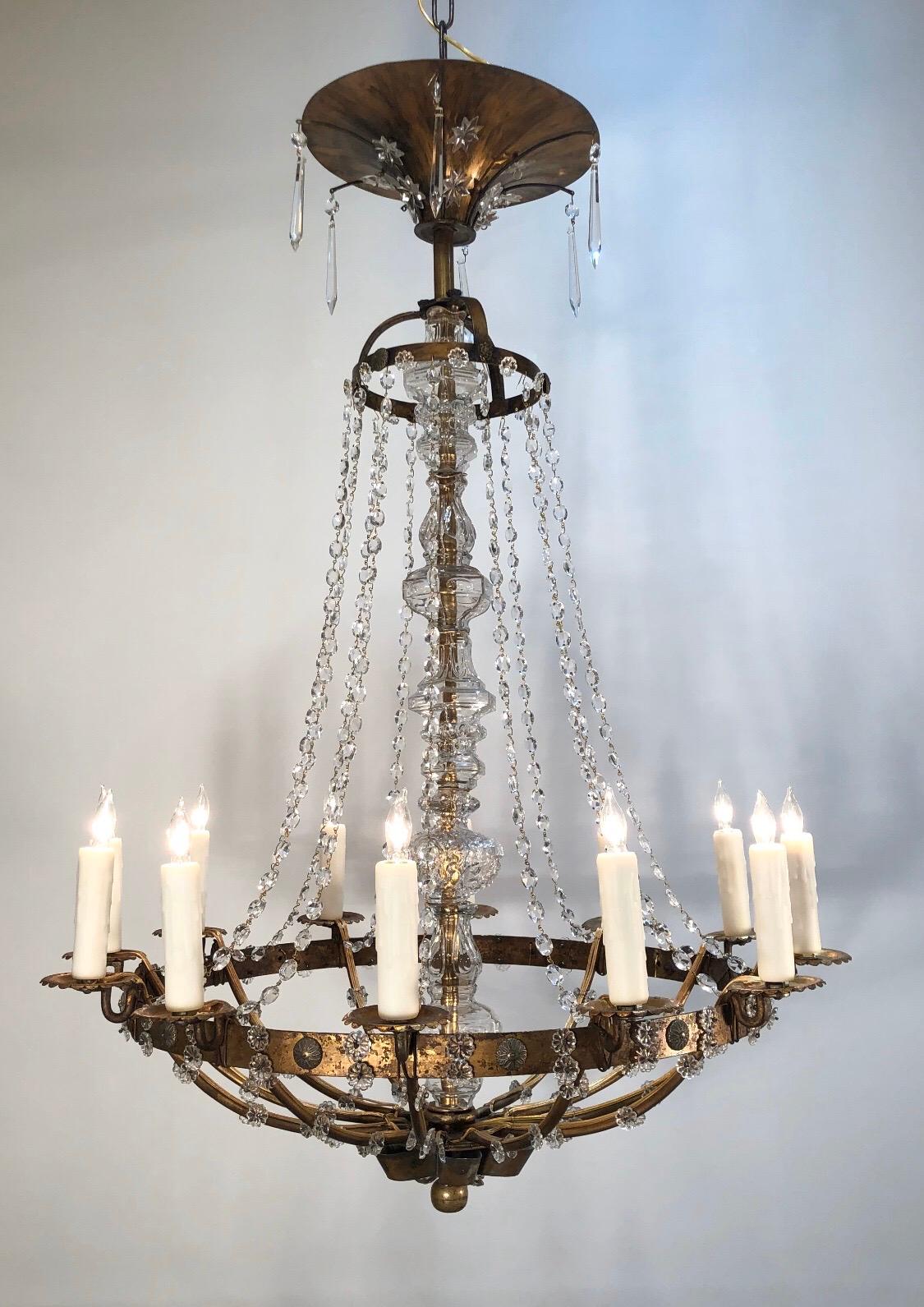 Elegant Italian neoclassical chandelier is gilt iron and tole with beautiful hand blown Venetian glass center stem and replaced crystal chains. The neoclassical chandelier has twelve lights that were originally candle.