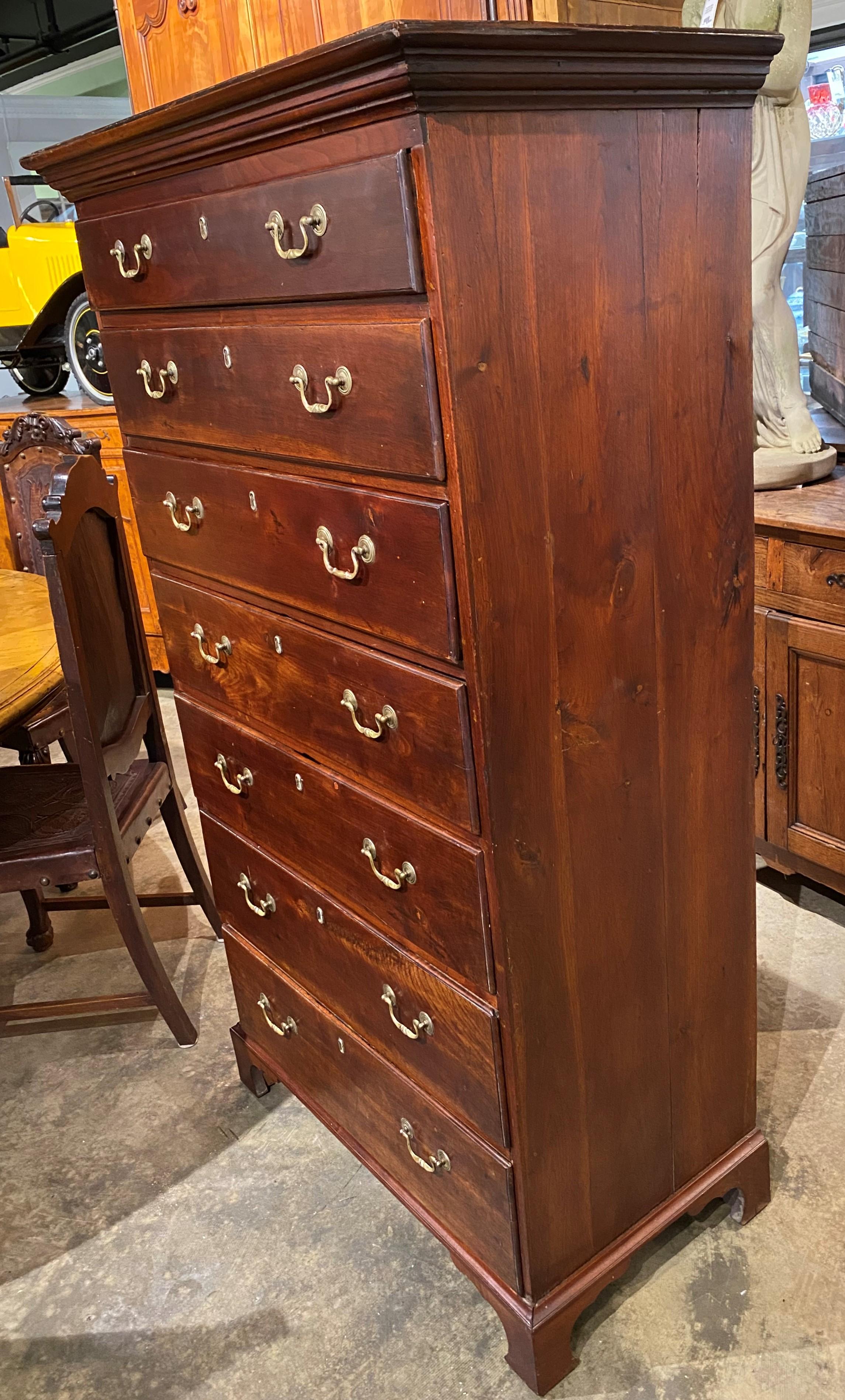 A nicely made hand carved walnut Chippendale style tall chest with most of its original color finish intact, with molded cornice surmounting seven graduated long drawers, each with replaced brasses, and original wide board back, all supported with a