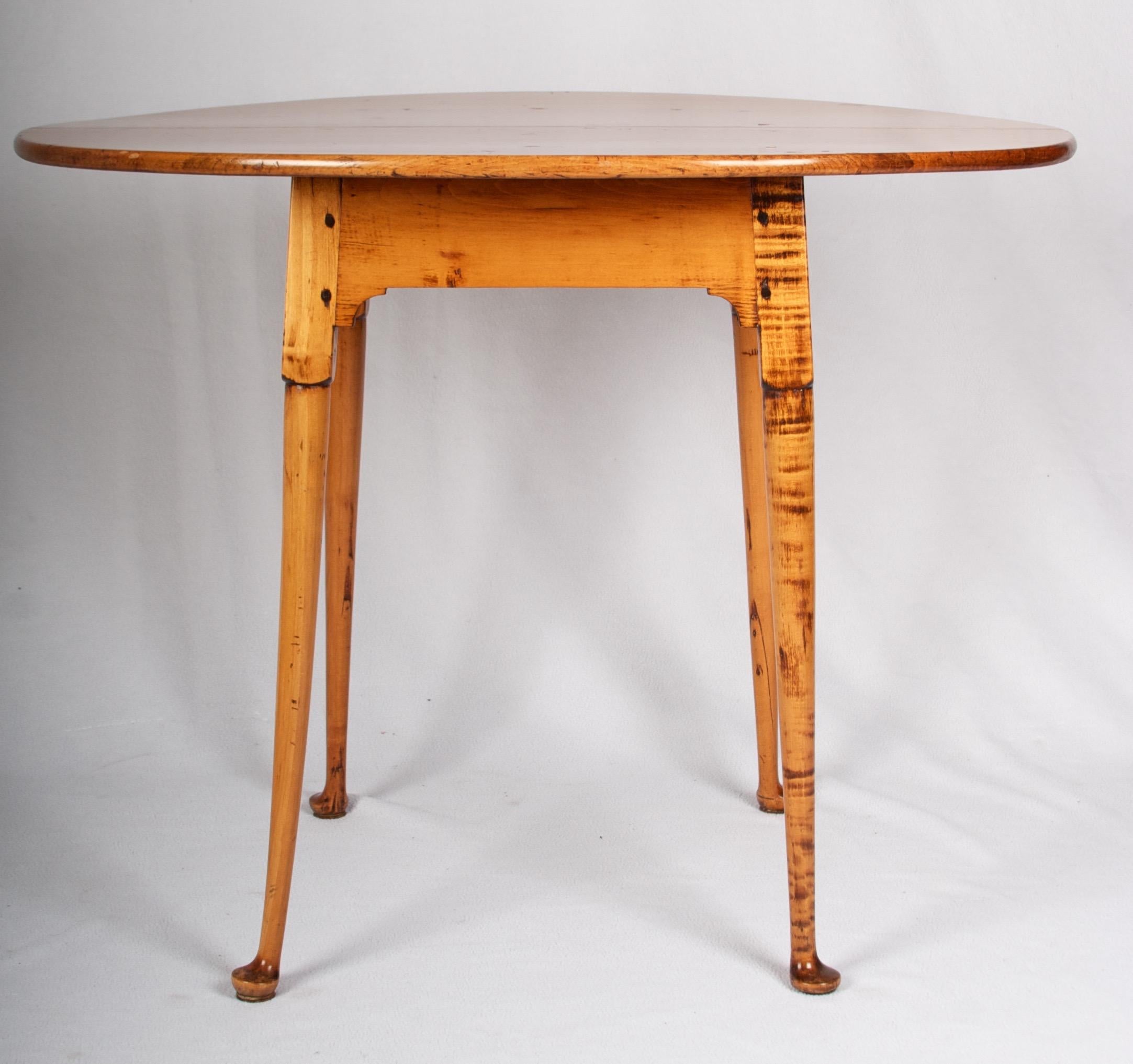A beautiful tiger maple tavern table from the late 18th century, handmade in New England.
The legs are pinned with dowels into the frame which supports a split oval top, cut from
choice maple, and affixed also with dowel pins - which are arranged