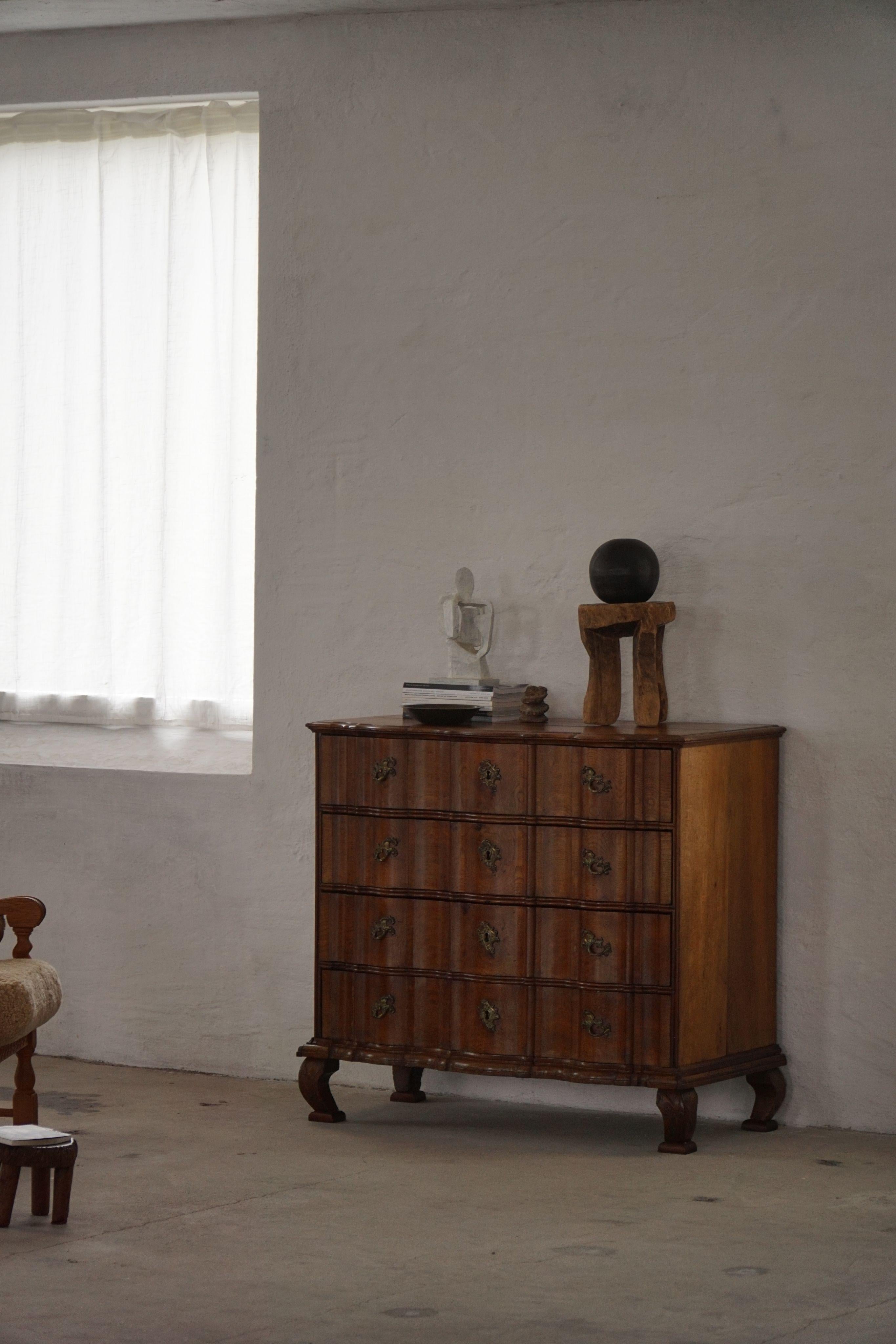 Une élégante commode baroque en chêne massif, fabriquée au XVIIIe siècle. La pièce présente une façade joliment incurvée et brisée, avec quatre tiroirs et une base amovible. La base repose sur des pieds avant en cabriole, mettant en valeur la