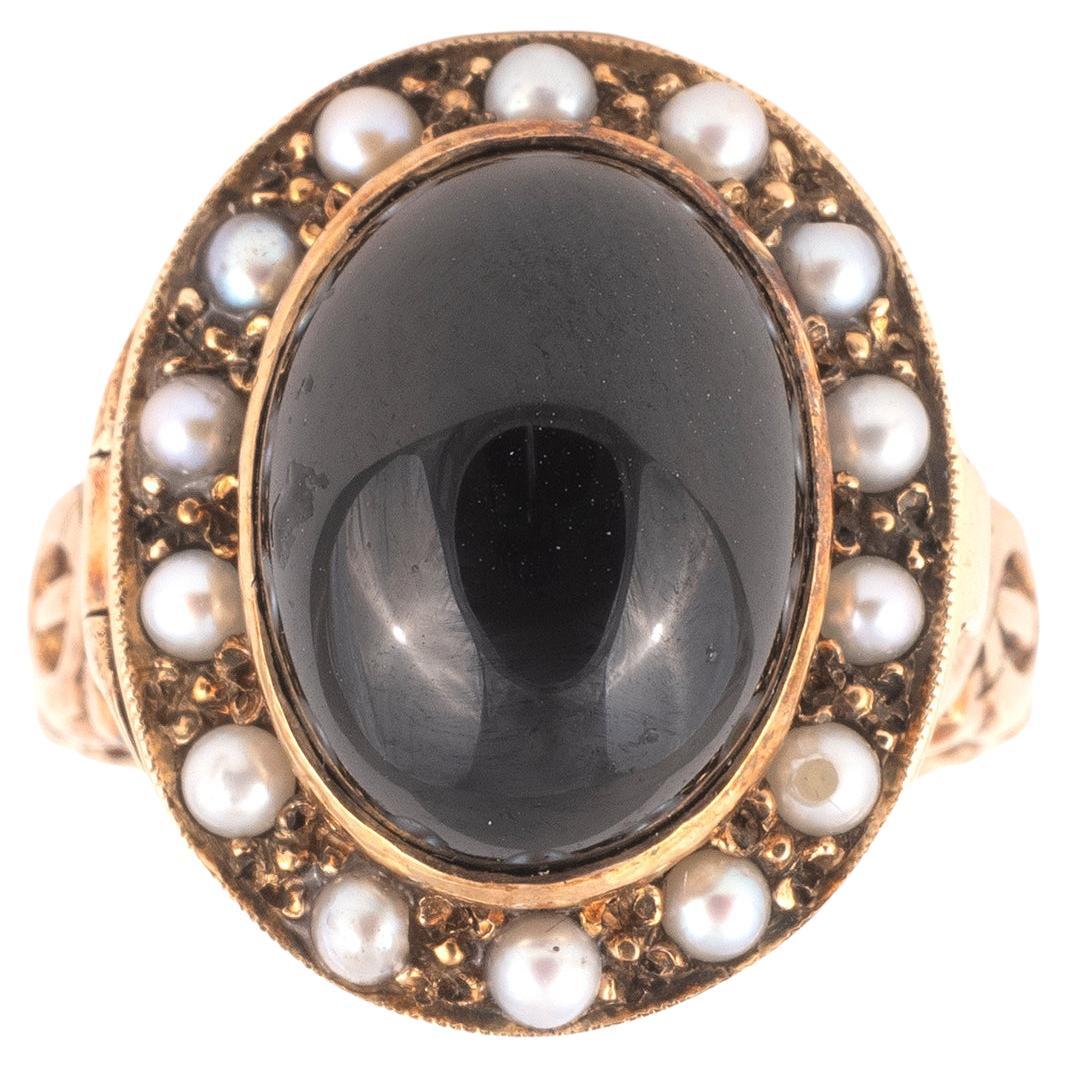 The bezel shaped as a hinged cluster set with an cabochon garnet and natural pearl revealing a small secret compartment, to a foliate trifurcated shoulders, mounted in gold.
The two-part ring face consists of a lid and catch that opens to reveal a