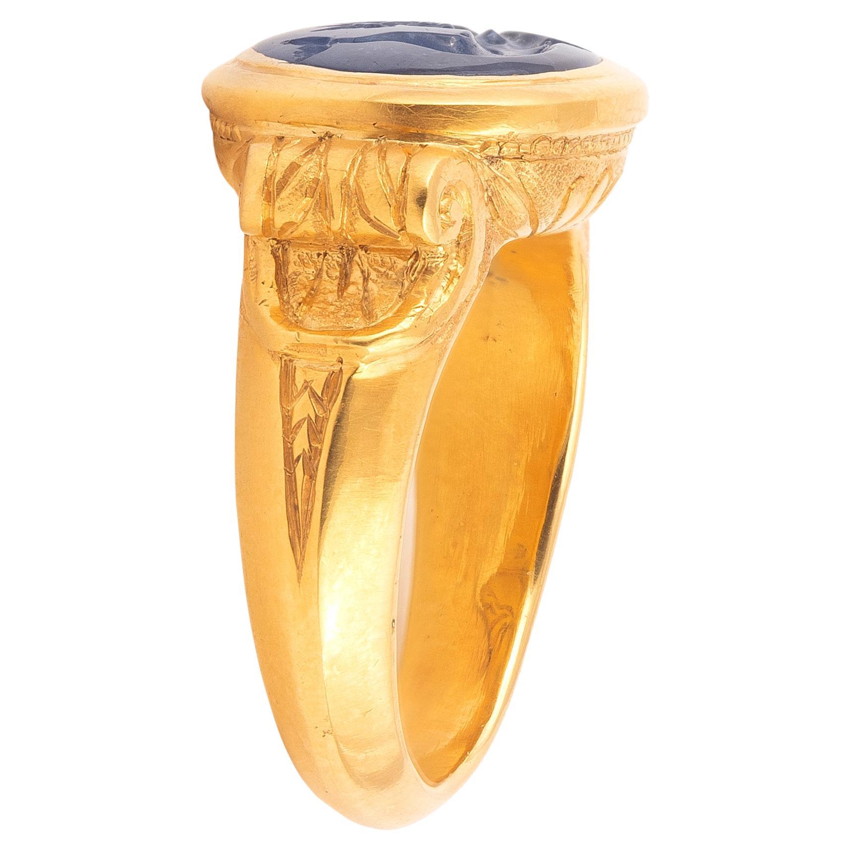 A Neoclassical carved sapphire intaglio, depicting Eros and Dolphin mounted in yellow gold. The top size is 21mm x 14mm; the finger size is 9 3/4 and the weight is 21 gr.