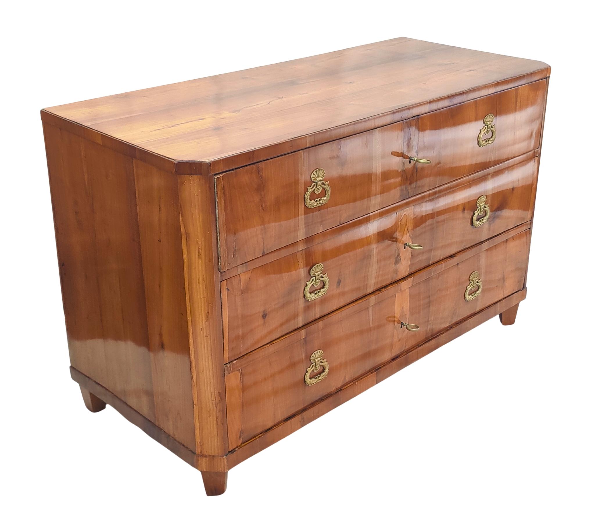 This late 18th century cherrywood commode, dating from around 1790, reflects the refined elegance of the Classical period. Crafted in solid cherrywood, the commode features three full-length drawers, each adorned with its original brass ring