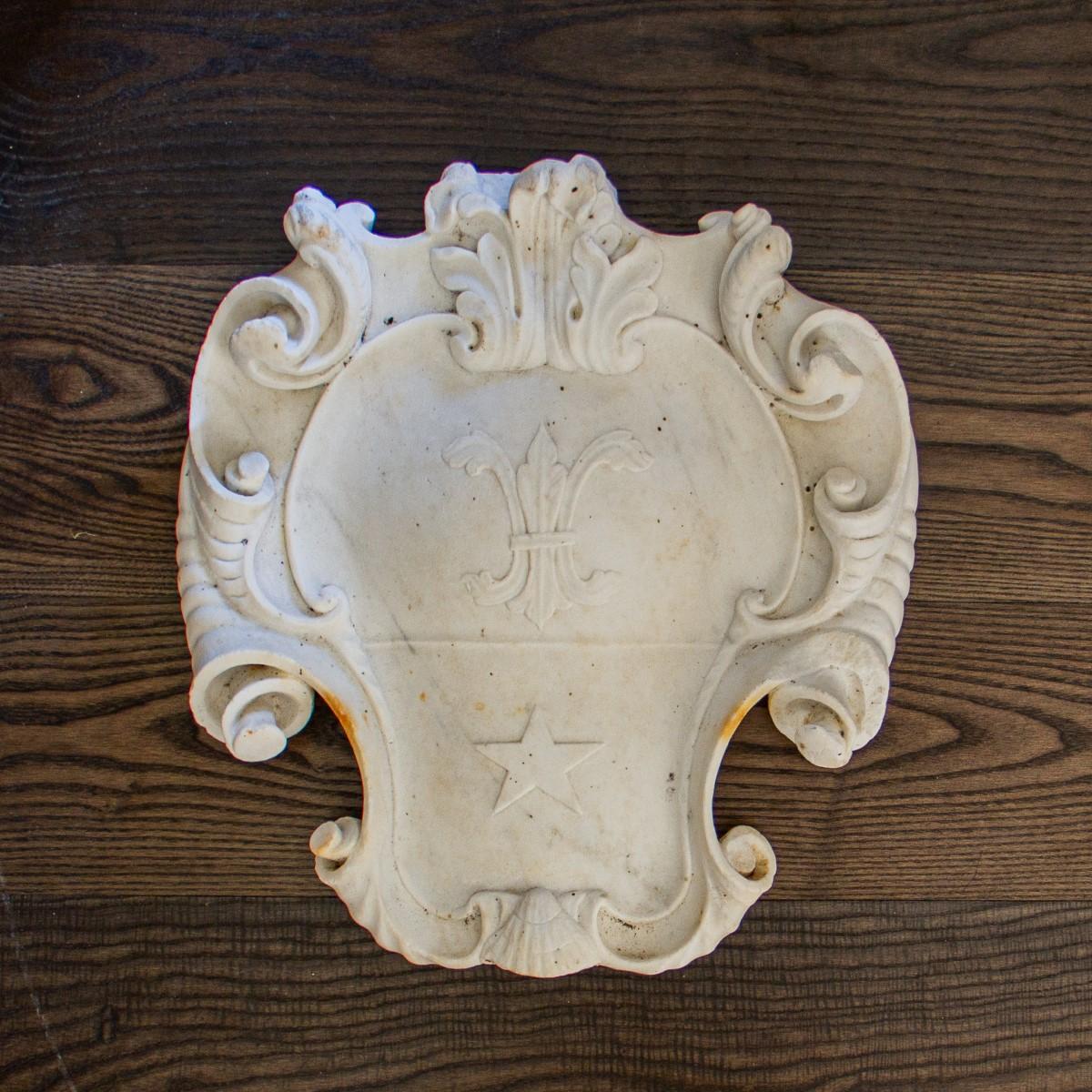 Late 18th century continental carved white marble cartouche or shield bearing a star and decorated with foliage and scrolling carvings.