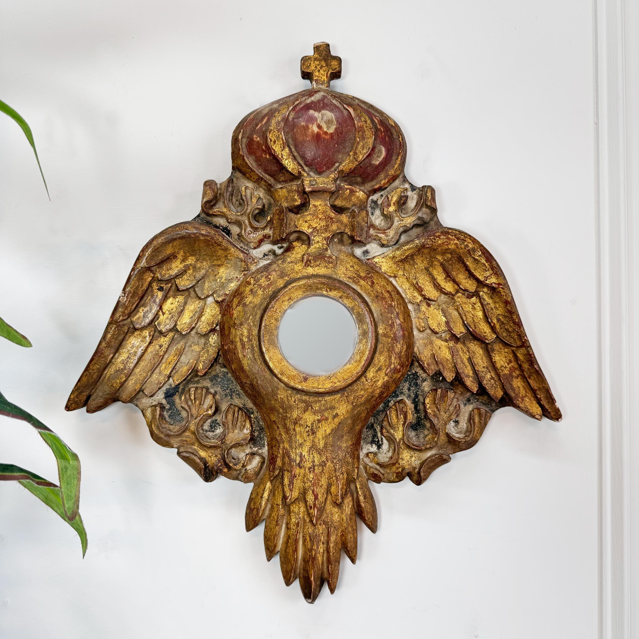 An exceptional decorative church mirror, in giltwood and gesso, France, late 1700’s.



The body in the form of a Dove, topped with a crown bearing the cross, in gold and red. To the centre a small circular mirror, the plate is later.



Height 45
