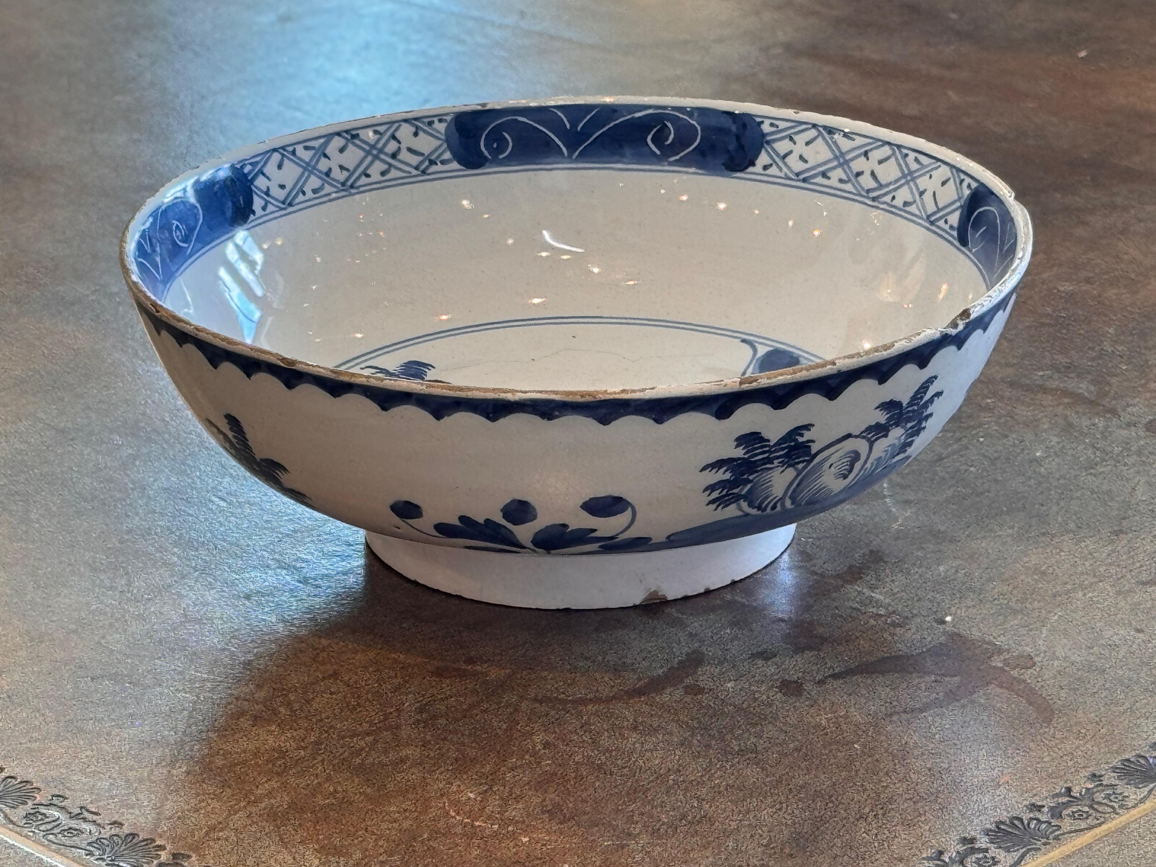 Une magnifique coupe de Delft peinte à la main représentant un paysage classique en bleu et blanc avec un paysage serein, des feuillages délicats et des motifs géométriques en bordure. L'extérieur présente des éléments décoratifs fluides qui