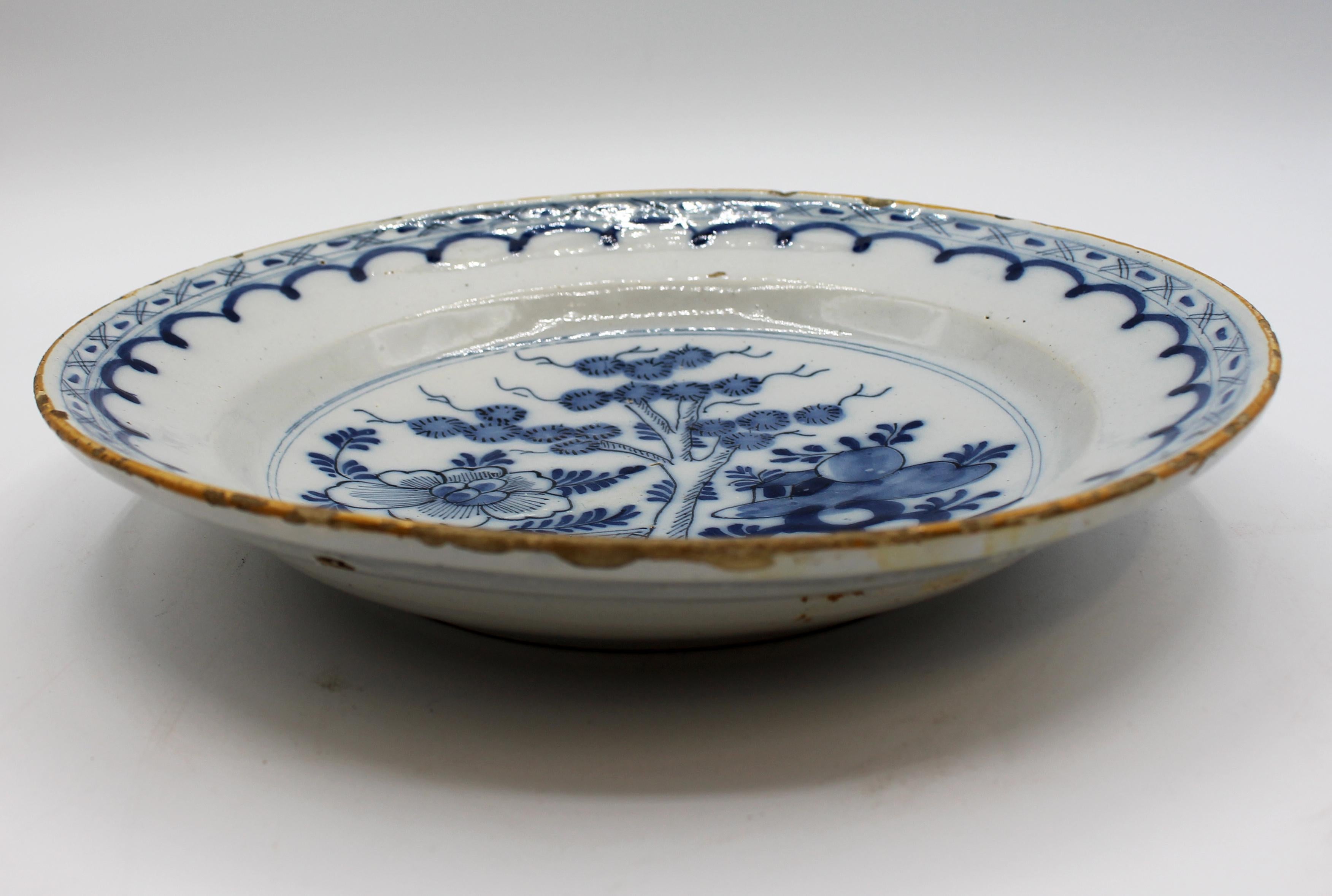 Late 18th century Delft blue & white deep chop plate. Central Asian influence garden scene with simple shaped repetitive border and yellow rim. Frits commensurate with material, age & use. 10.25