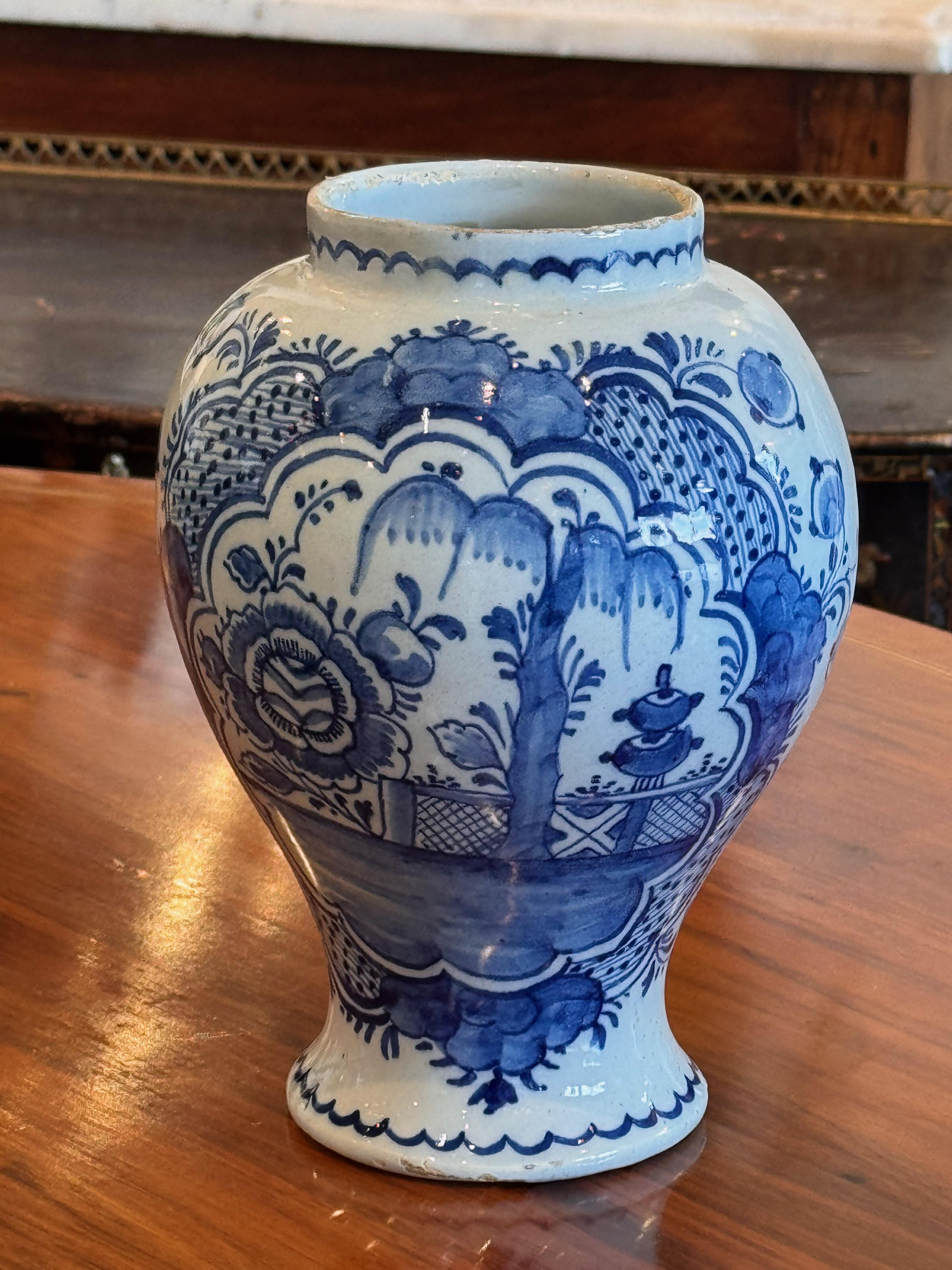 Jarre de Delft finement décorée de motifs floraux et paysagers en bleu et blanc peints à la main. La forme gracieuse et bulbeuse est complétée par des motifs festonnés et des détails ornementaux délicats, mettant en valeur le savoir-faire