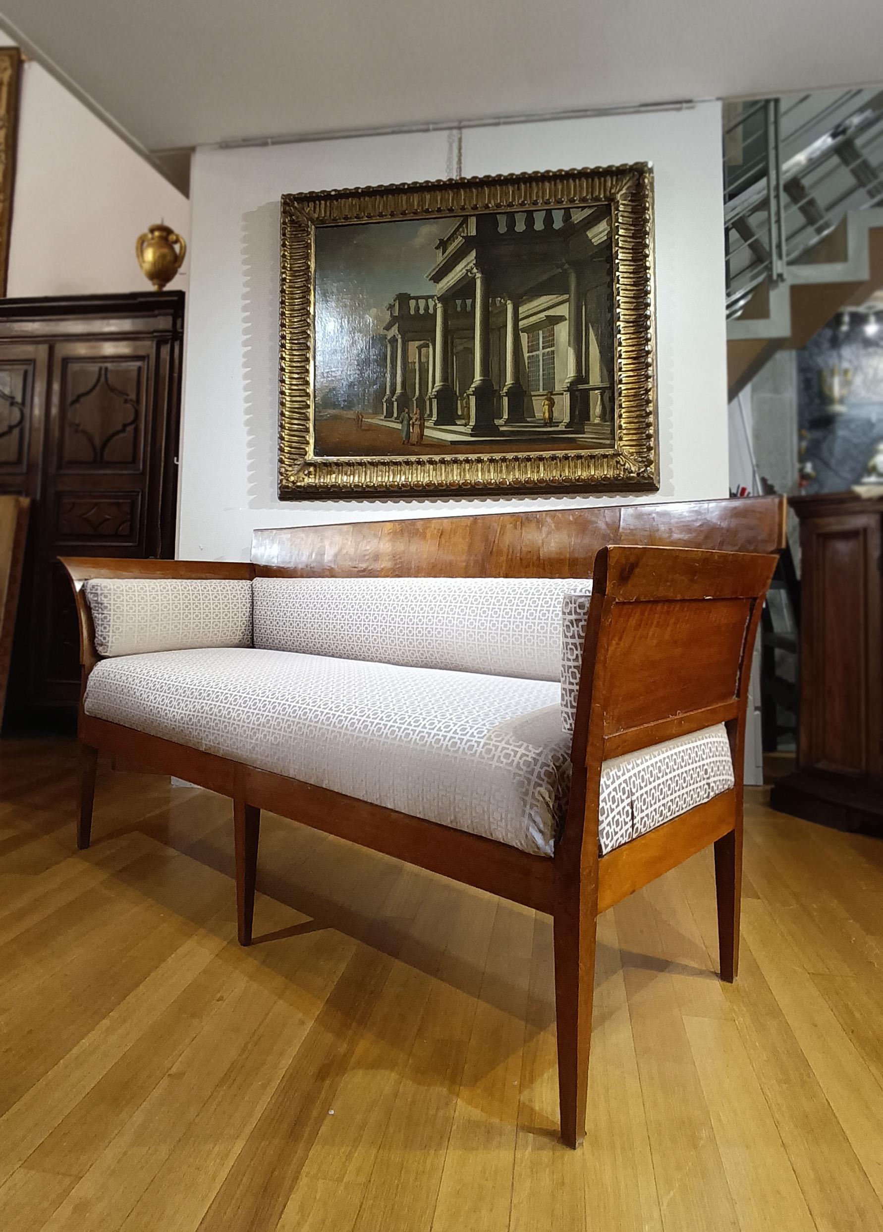 An elegant, compact sofa, crafted from solid walnut and veneered walnut. The sofa features truncated pyramid legs, typical of the period, and flared armrests that lend elegance and break up the linearity of the shape. Partial padding, found in the
