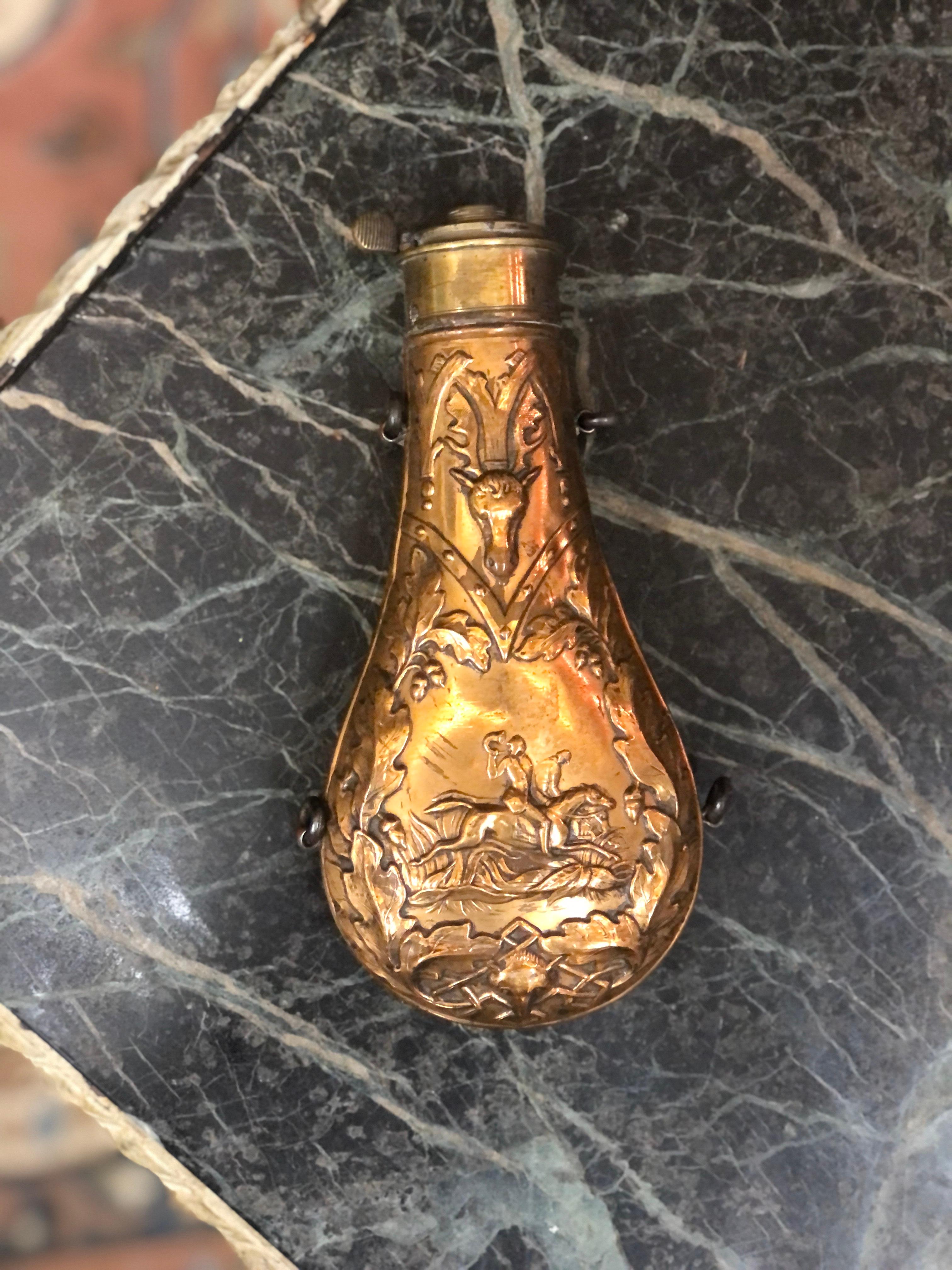 Antique Embossed Brass Powder Flask – Hunting Scene Design

This is a beautifully crafted 18th-century brass powder flask, featuring an ornate embossed hunting scene. The front showcases a finely detailed stag head and oak leaf motif, symbolizing