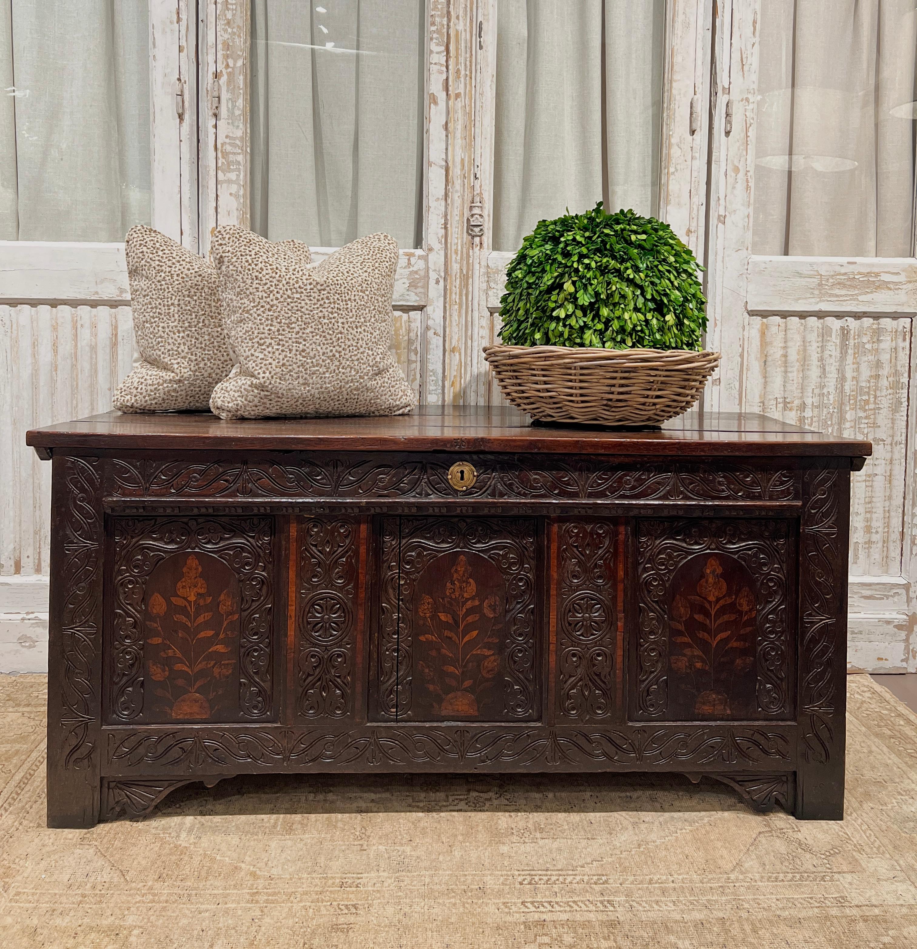 circa late 18th - early 19th century, England.

This stunning antique oak blanket chest/coffer is truly a work of art. The front side features three beautiful floral inlays surrounded by intricately hand-carved details, a brass center (lock) and