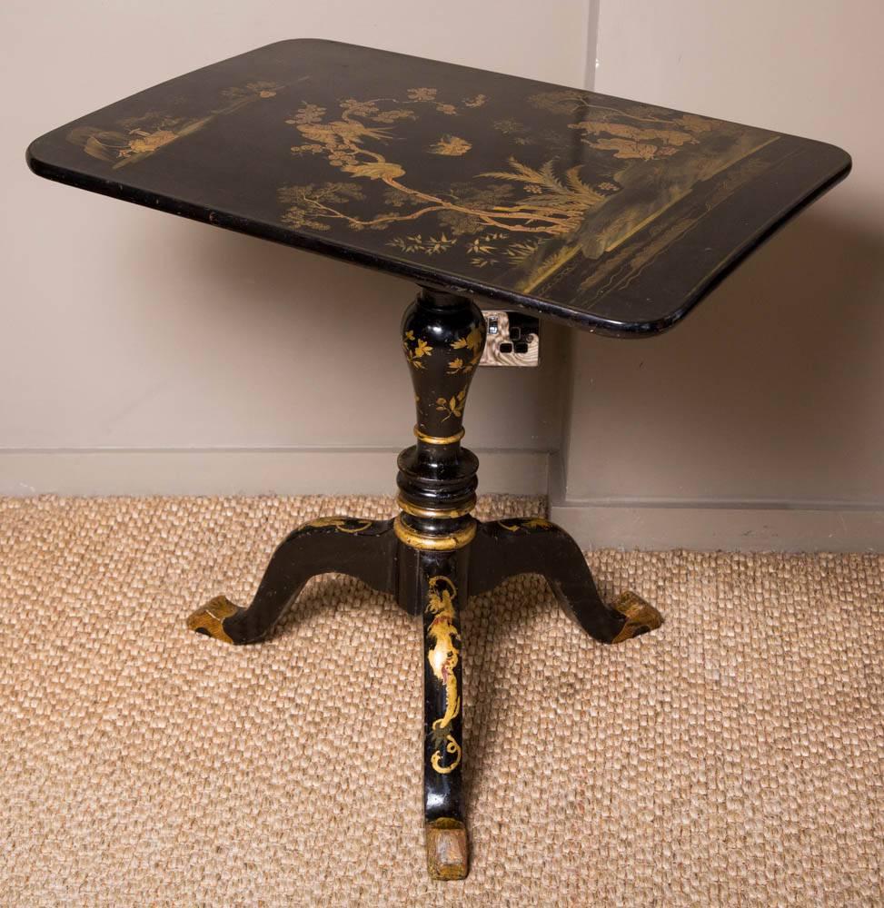 A handsome and extremely decorative English late 18th century Japanned black rectangular tilt top chinoiserie side table. The table is raised by a richly painted tripod base with gilt designs of foliate scrolls on a black lacquered background, circa