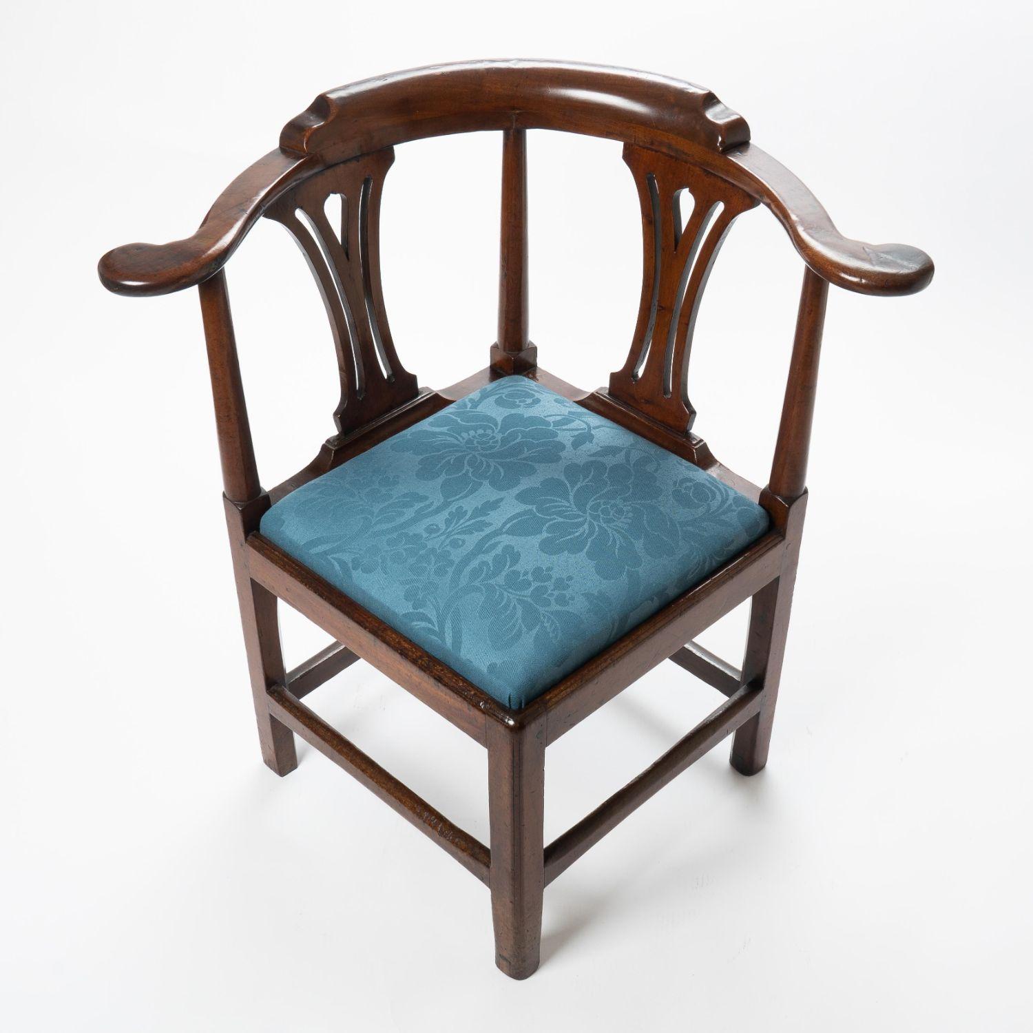 George III mahogany corner chair upholstered with a slip seat in blue marine wool. The legs are square with beaded corners, and the crescent shaped crest rail is supported by pierced back splats and turned posts at the scroll arm