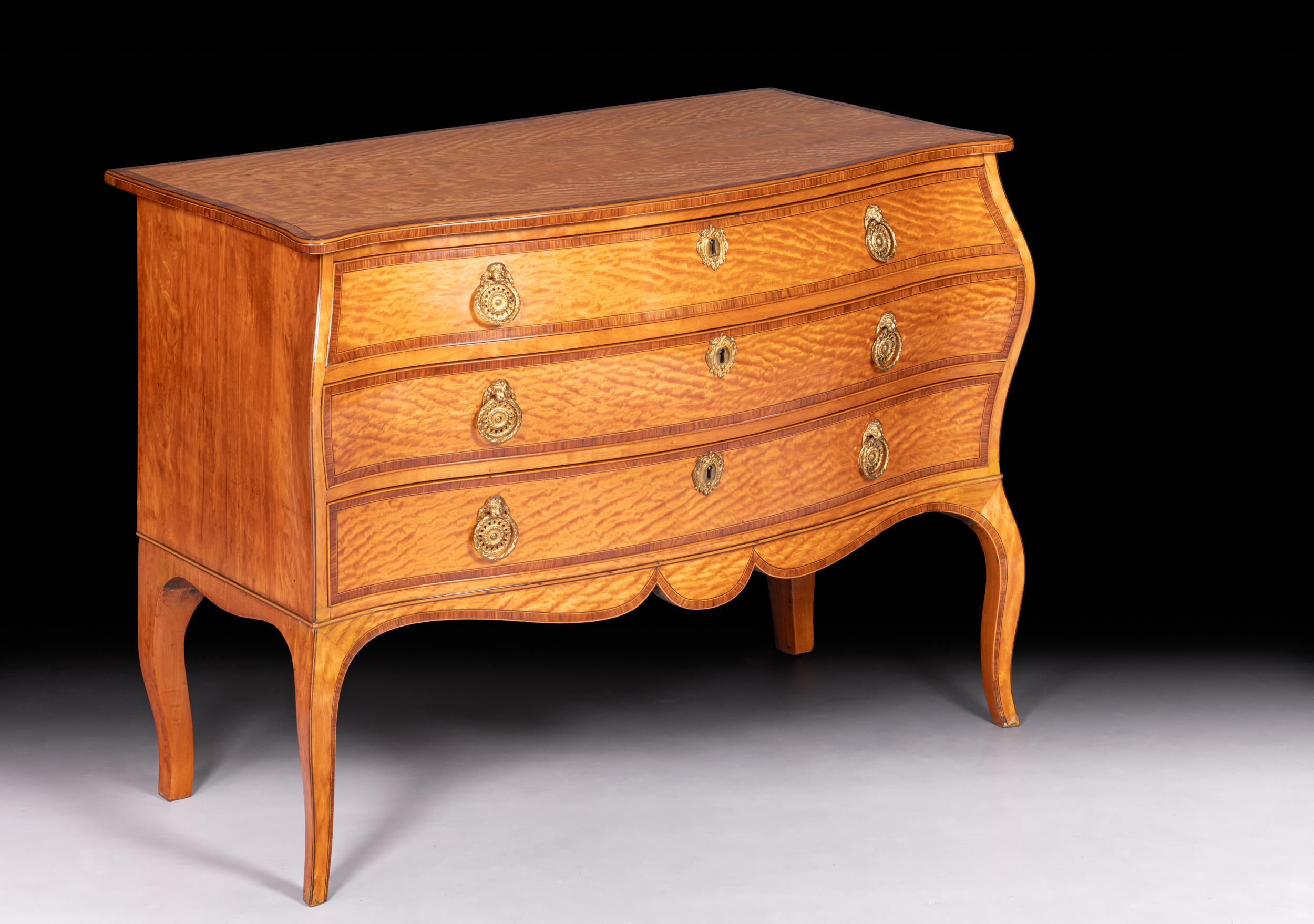 An exceptional George III Satinwood serpentine shaped commode, the serpentine top with out-swept front corners cross-banded in kingwood. The kingwood moulded border frame around central panels of book-matched satinwood veneers, above three graduated