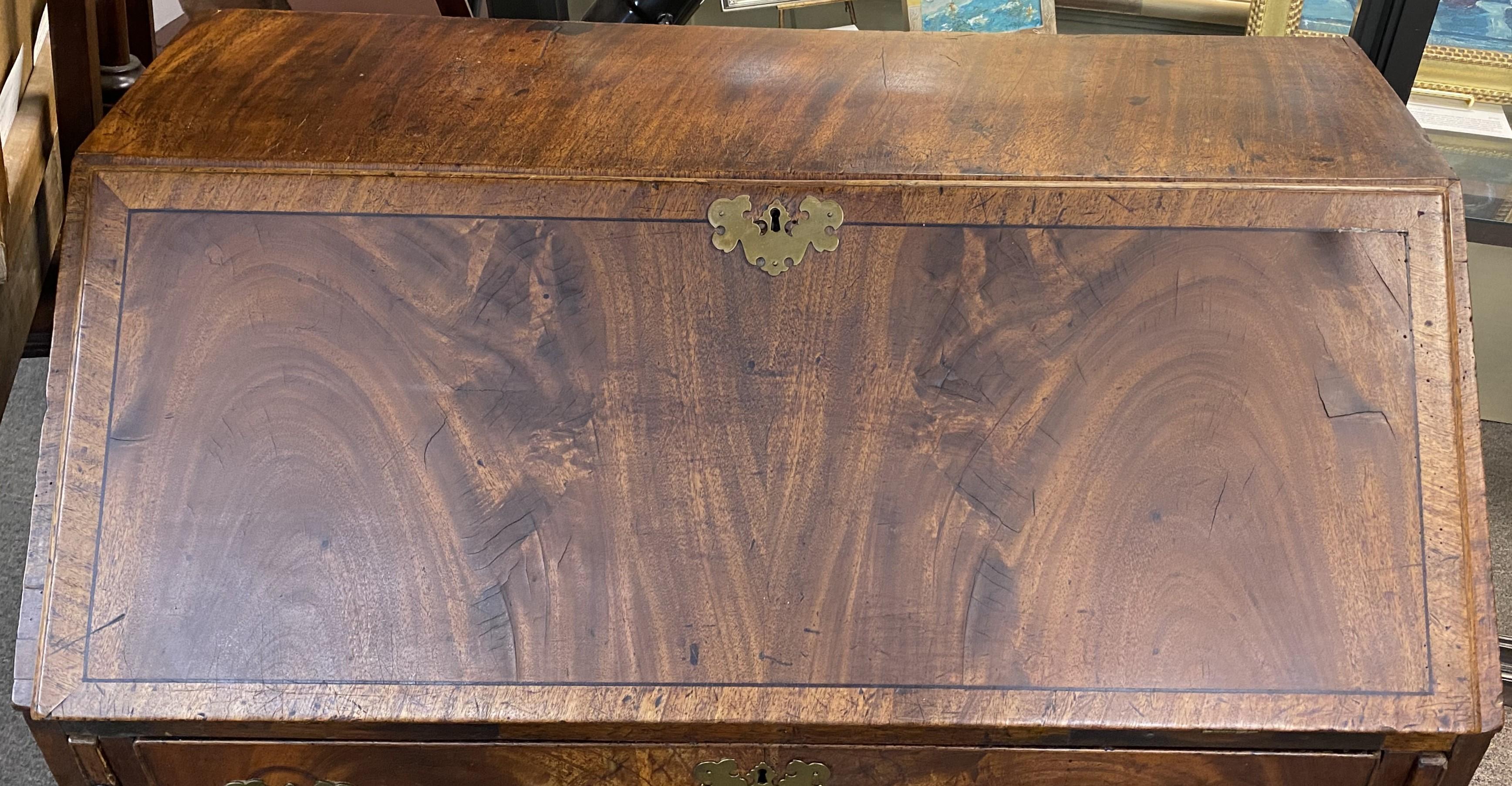 A good example of a Chippendale slant front desk with bookmatched figured mahogany veneers, a slant front which opens to a compartmentalized interior with fitted drawers and cubbies, over four long drawers, each with replaced batwing brasses, all