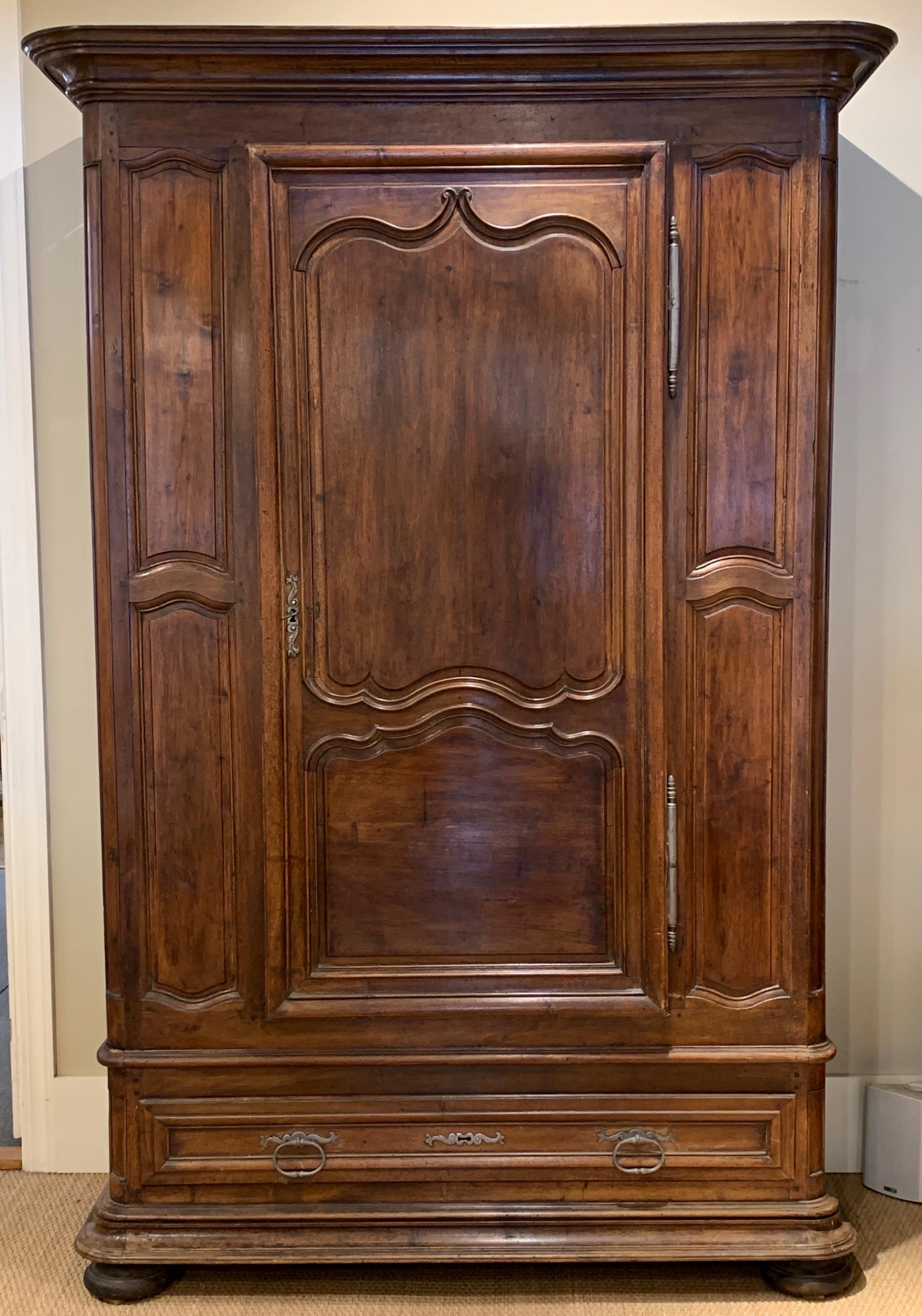A late 18th century French heavily carved walnut armoire with single-door opening to reveal three shelves over a low single drawer all with original iron hinges, pulls and locks. The piece displays a beautiful carved crown and all rests on large bun