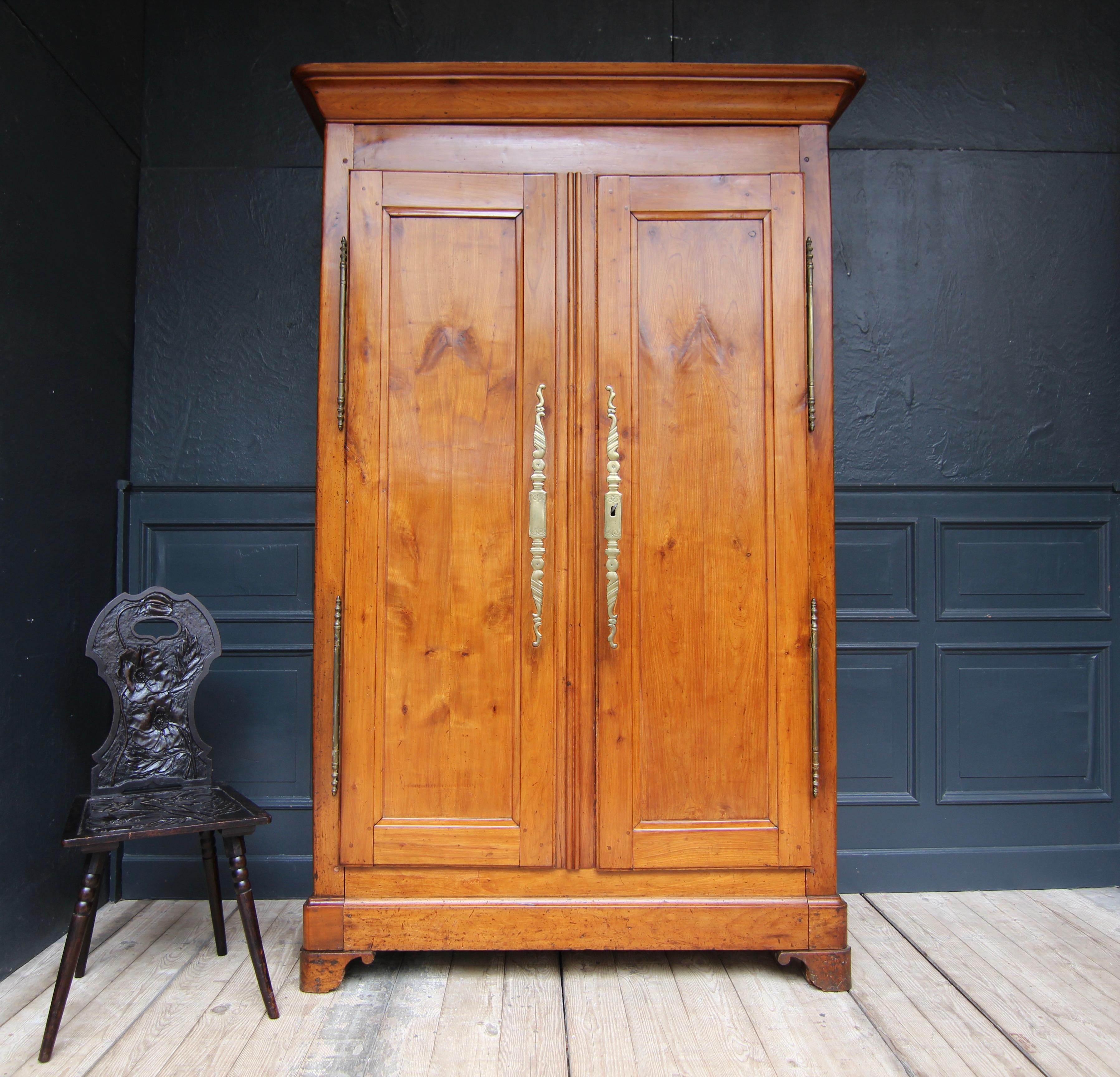 A late 18th century French cabinet solidly made of cherry wood.

Simple two-door body with coffered sides and profiled, slightly rounded cornice. Two doors in frame construction hung on large hand-forged brass fittings on the outside.

Fitted
