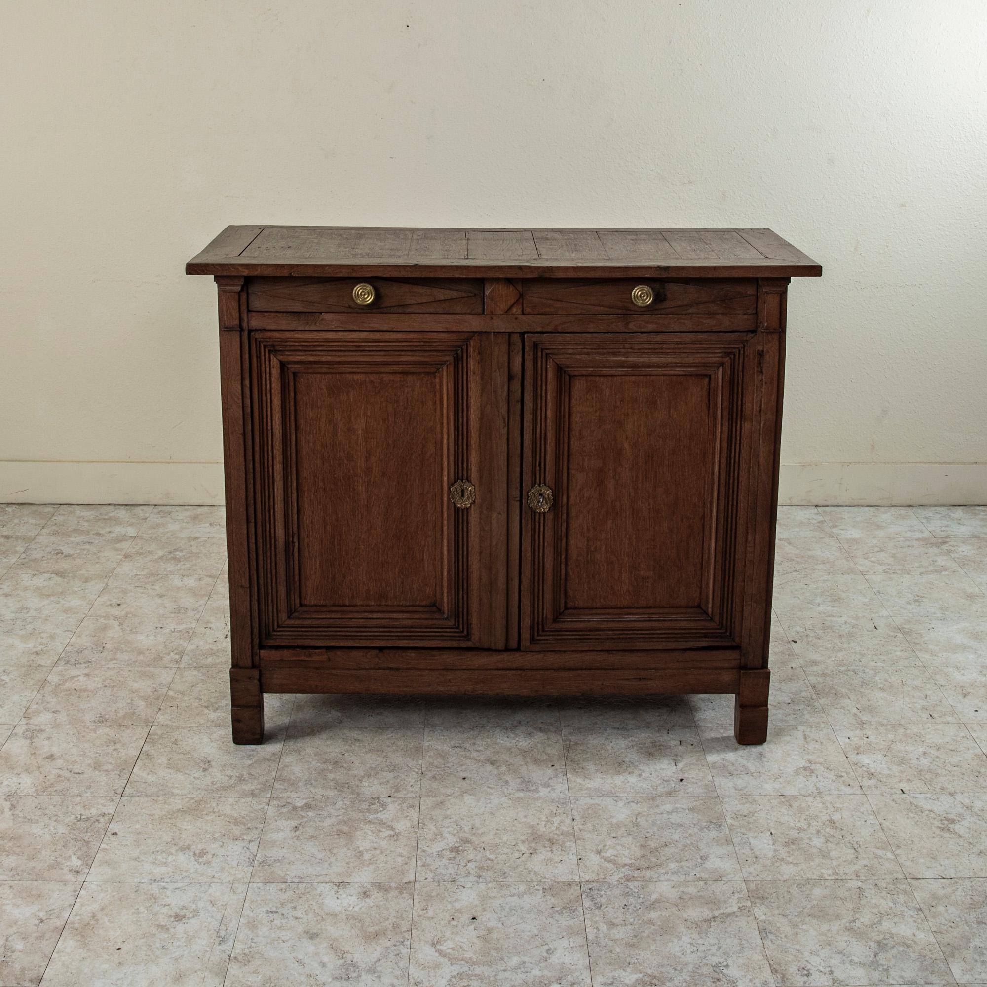 Found in Normandy, France, this late 18th century Directoire period solid oak buffet features half columns at the corners flanking its two doors. Two drawers of dovetail construction are appointed with bronze drawer pulls detailed with spiral