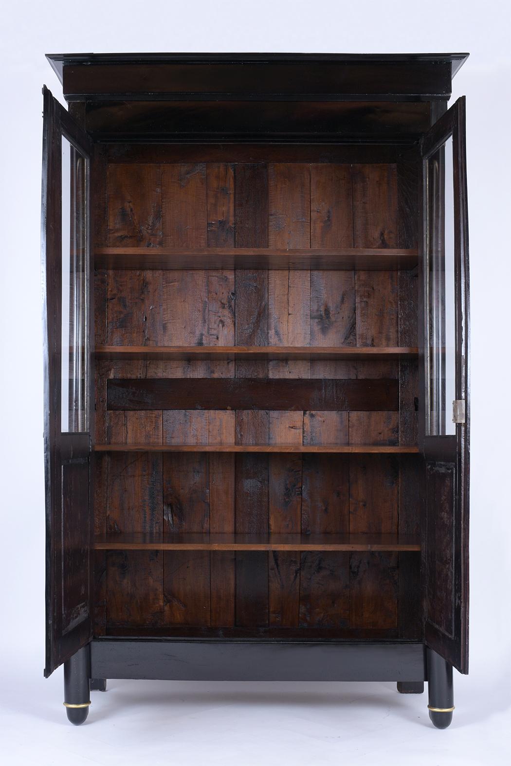 This French late 18th century double door bookcase is made out of mahogany wood newly stained in an ebonized color with gilt molding accents and polished lacquered finish. This elegant Empire style display features two doors with clear glass on the