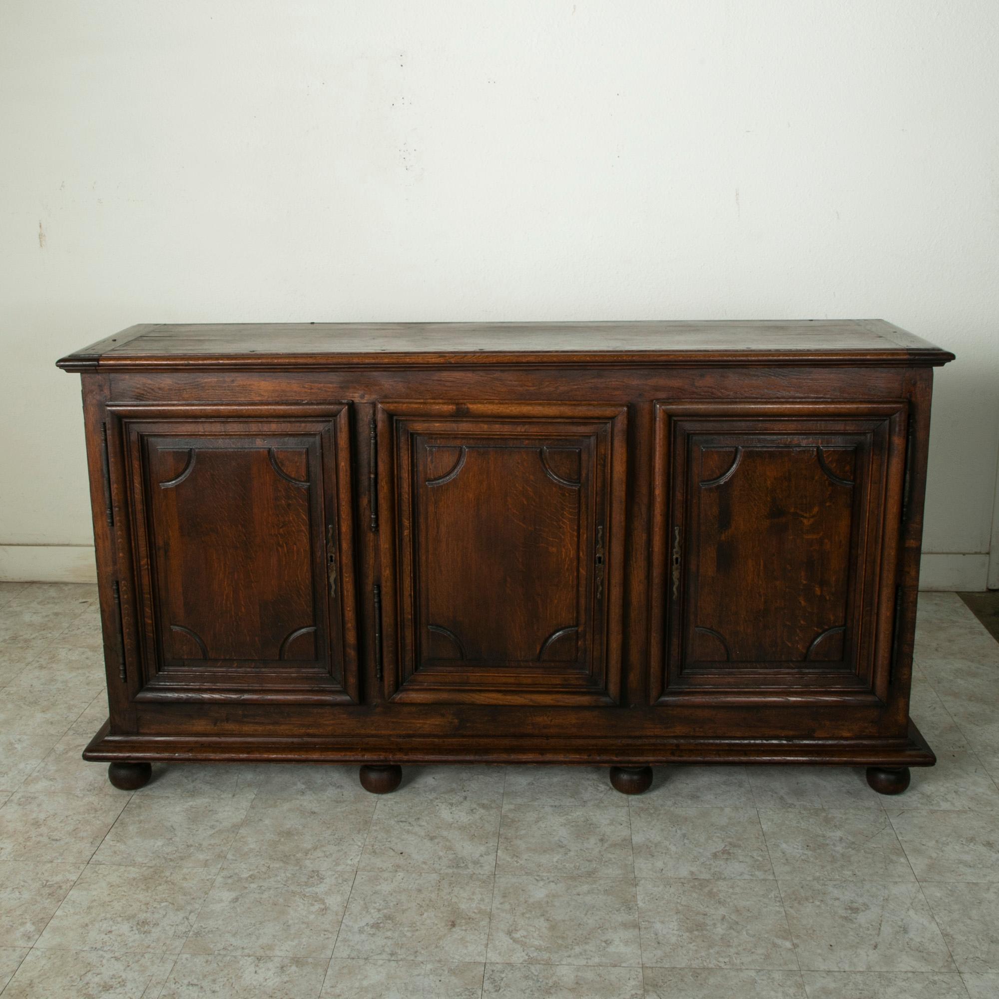 This late eighteenth century French oak enfilade features hand pegged paneled sides and doors, and a beveled top. its three doors display Louis XIV design elements with symmetrical rectangular panels. Behind each door is a single drawer of dovetail