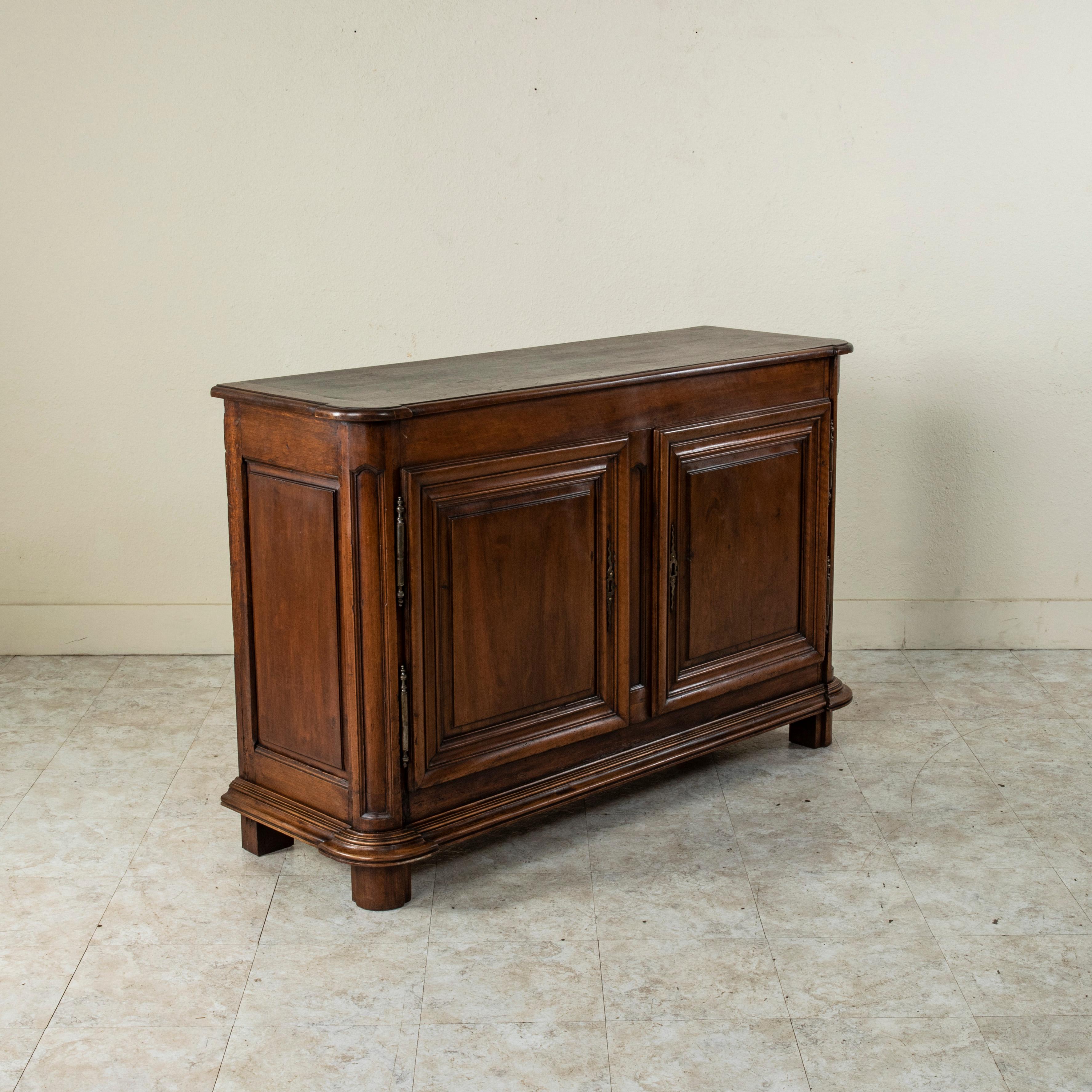 This late 18th century French walnut buffet or sideboard features hand pegged paneled sides and and a beveled top. Its two doors are classic Louis XIV designs with symmetrical rectangular panels. The doors open to reveal a single interior shelf that