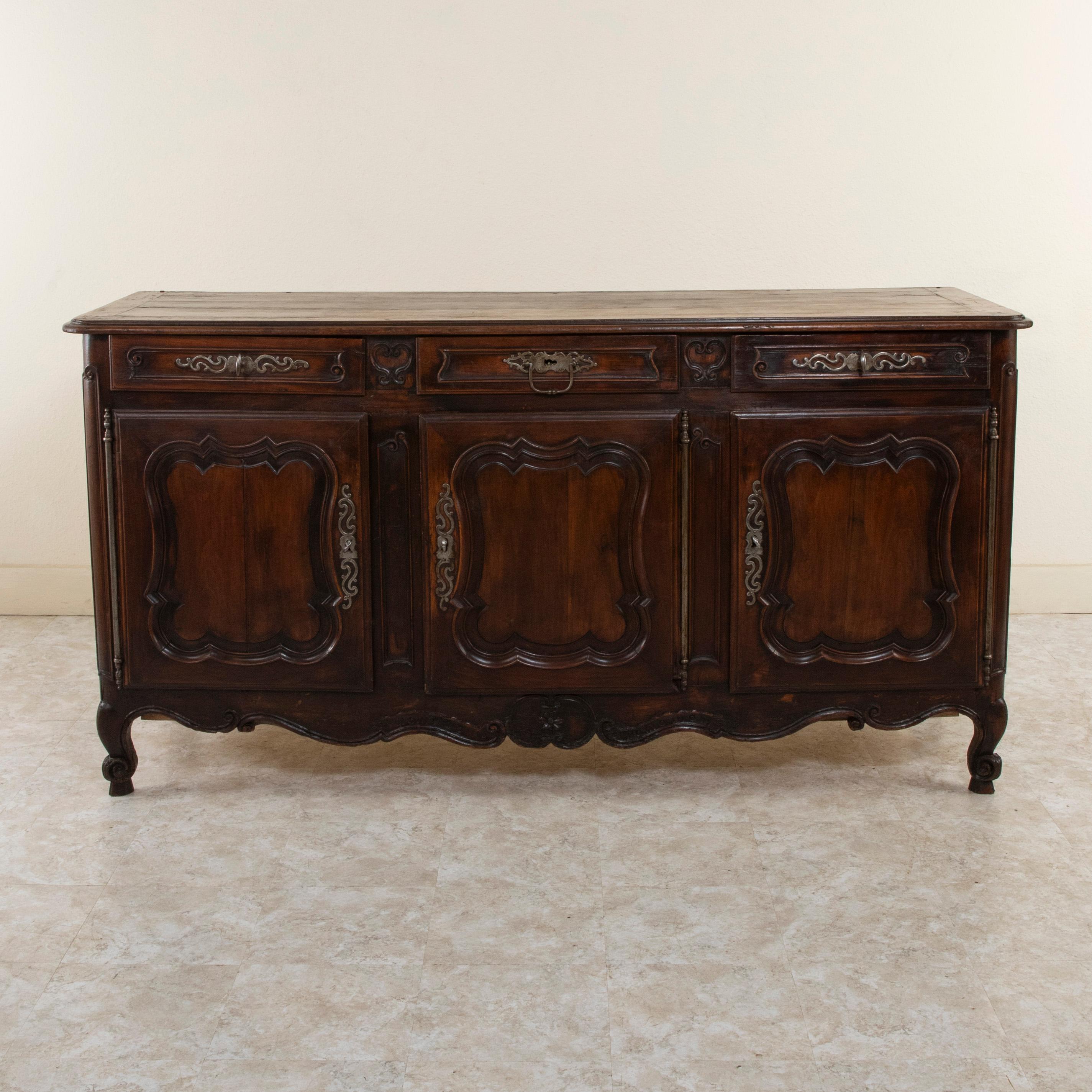 This late eighteenth century Louis XV style oak enfilade or sideboard features paneled sides and doors, and hand-carved scrolling. A carved floral motif adorns the lower apron. The back of the piece is also all hand hewn. Resting on classic