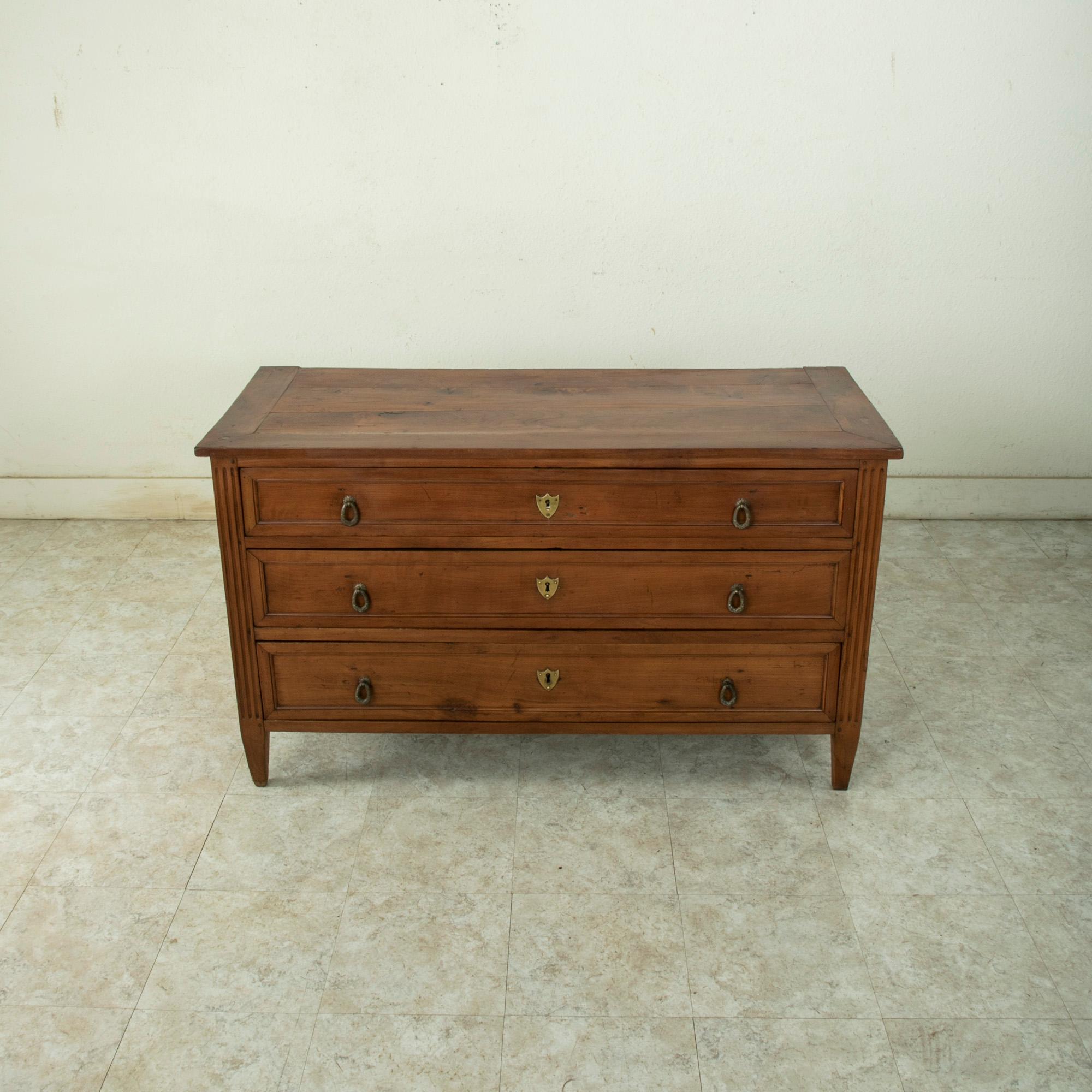 This late eighteenth century French Louis XVI period commode or chest is constructed of solid hand pegged cherry wood. The corners are detailed with hand carved fluting and terminate in tapered square legs. Its three drawers of dovetail construction