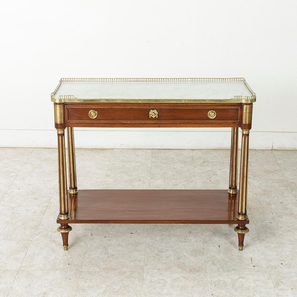 This late 18th century French Louis XVI period mahogany console table features a white marble top surrounded by a pierced bronze gallery. Bronze beading details the front and side panels and striated bronze plaques adorn the corners. A single drawer