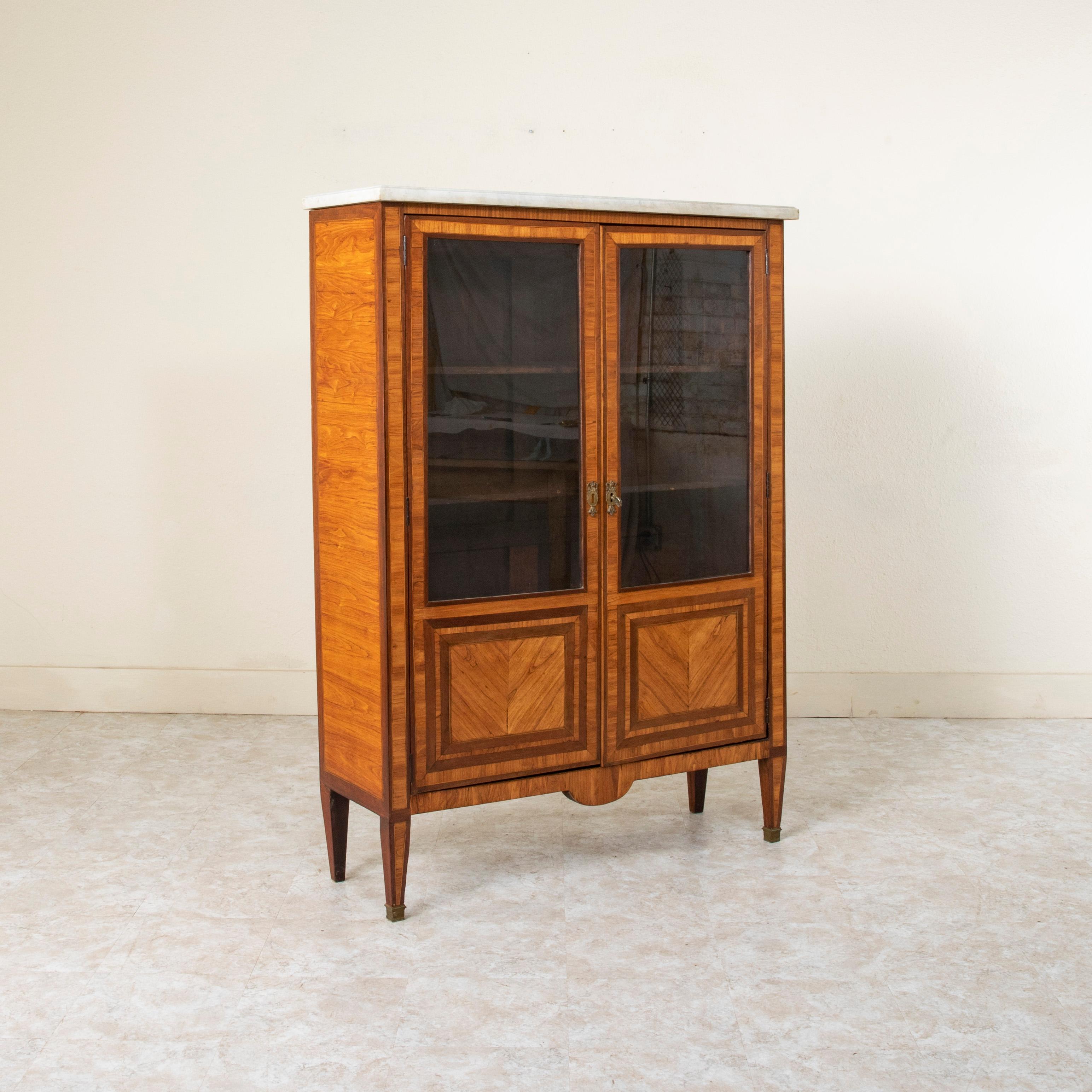 This small scale late eighteenth century Louis XVI period walnut marquetry vitrine or bookcase features rosewood borders on each side with fine lines of lemon wood inlay forming inset borders. Its two glass doors are fitted with book matched walnut